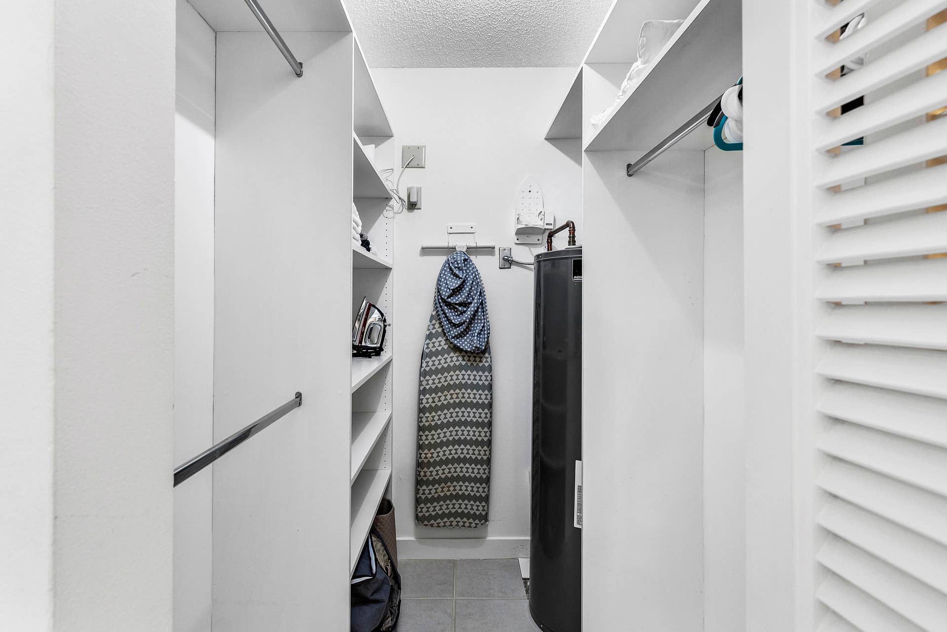 526 Club Drive, Palm Beach Gardens, FL 33418 Walk-in closet featuring white built-in shelving, dual hanging rods, tile flooring, and louvered double doors
