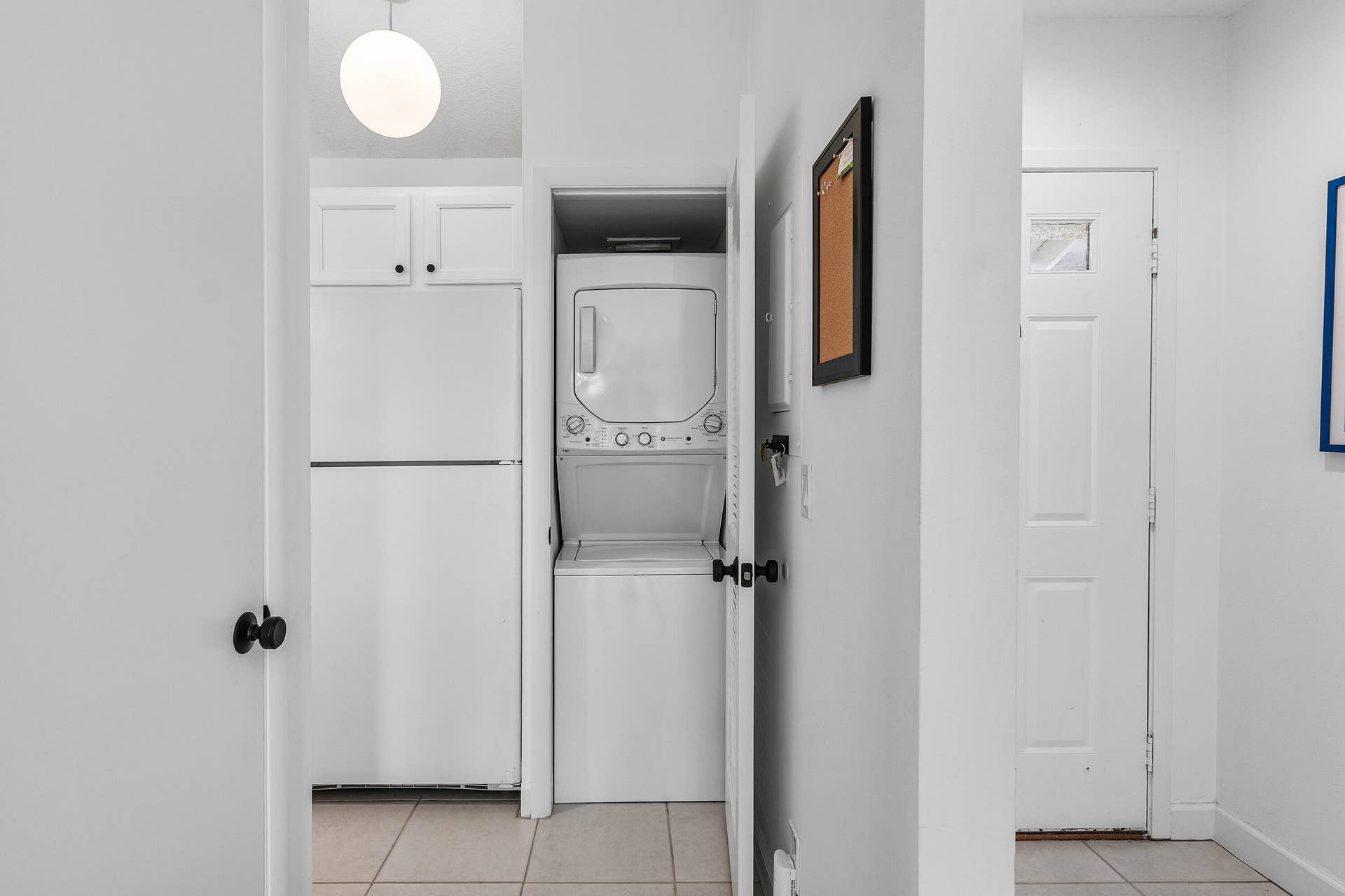 526 Club Drive, Palm Beach Gardens, FL 33418 Utility area featuring stacked laundry appliances, white cabinetry, ceramic tile flooring, and a globe pendant light fixture