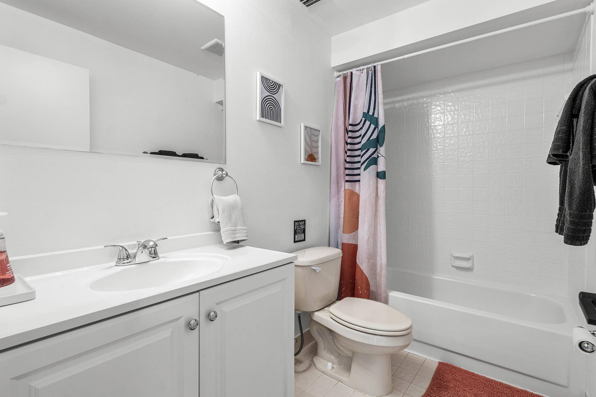526 Club Drive, Palm Beach Gardens, FL 33418 Bathroom featuring a white vanity cabinet, solid-surface countertop with an integrated basin, wall-mounted mirror, and a tub-shower combination with tile surround