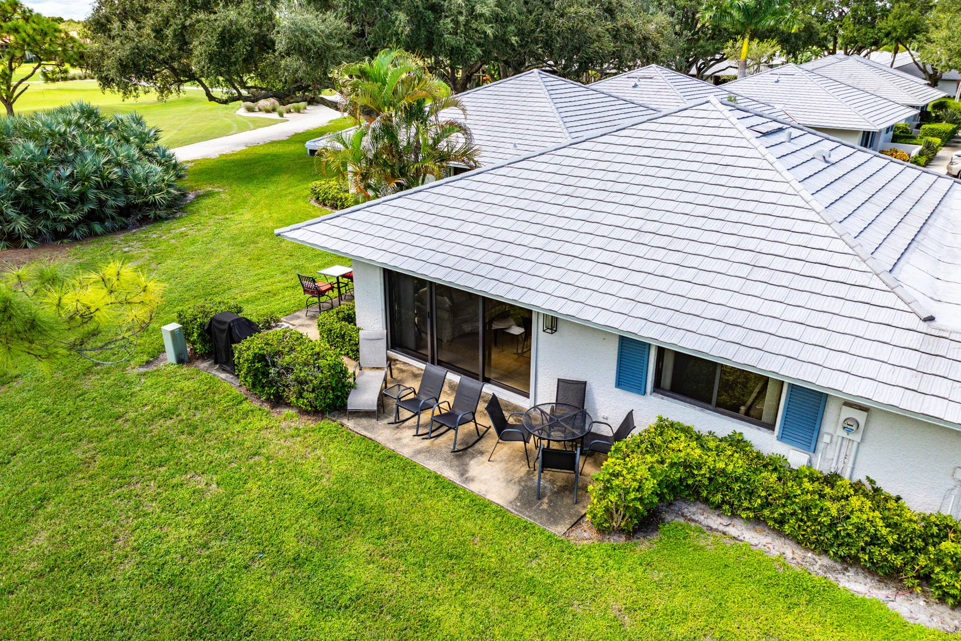526 Club Drive, Palm Beach Gardens, FL 33418 Exterior featuring a concrete tile roof, light-colored stucco siding, blue shutters, and a rear concrete patio