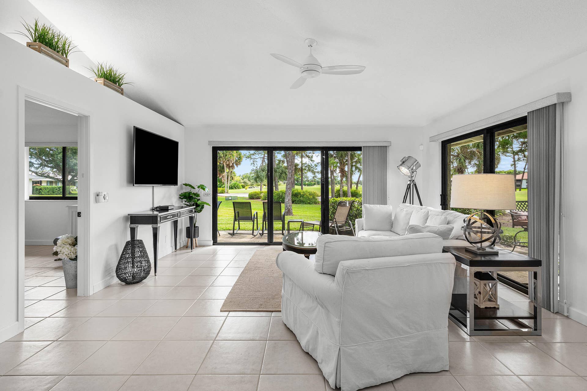 526 Club Drive, Palm Beach Gardens, FL 33418 Living area featuring light-colored tile flooring, a vaulted ceiling with a white overhead fan, and two sets of sliding glass doors