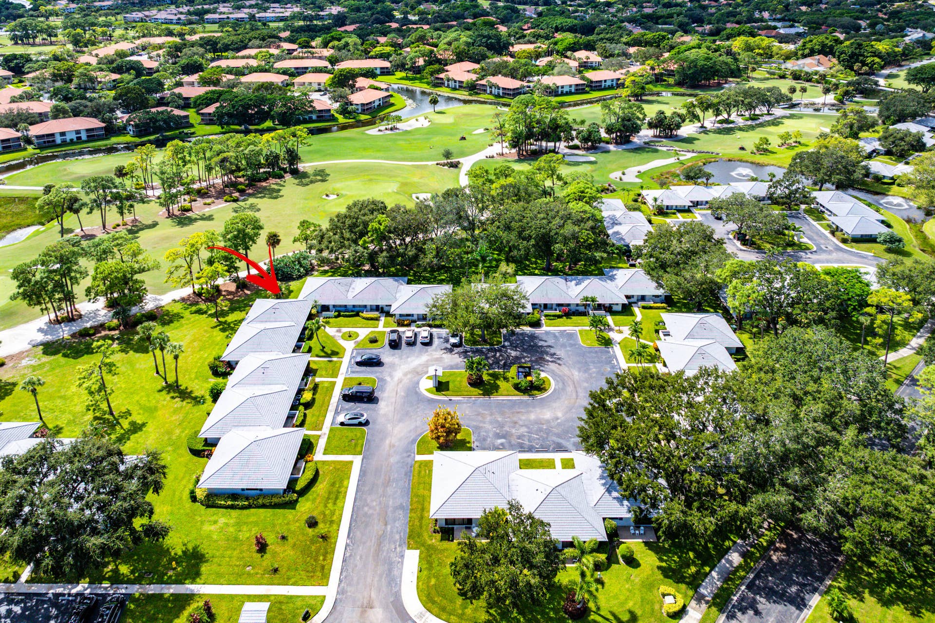 526 Club Drive, Palm Beach Gardens, FL 33418 Aerial perspective of residential structures featuring multi-slope hip roofs, surrounding green space, paved parking areas, and mature landscaping