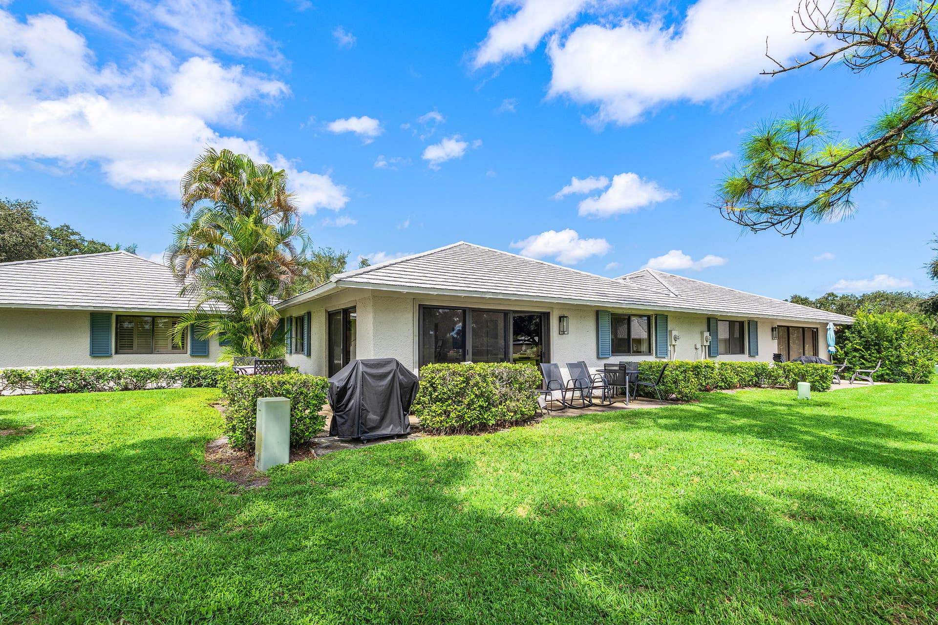 526 Club Drive, Palm Beach Gardens, FL 33418 Exterior facade featuring a hipped roof, stucco siding, sliding glass doors, and window shutters set against a manicured lawn