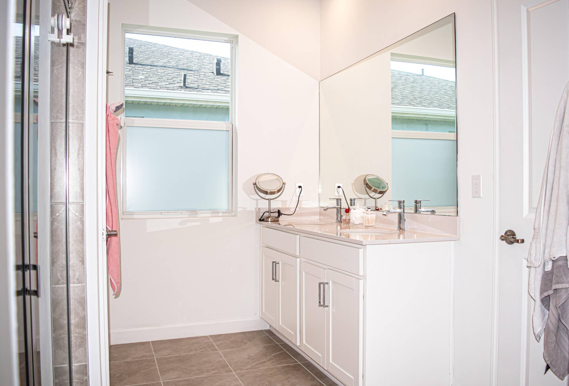 10317 SW Phineas Lane, Port St Lucie, FL 34987 Dual-sink vanity with light-toned countertop, large wall-mounted mirror, ceramic tile flooring, and frosted window