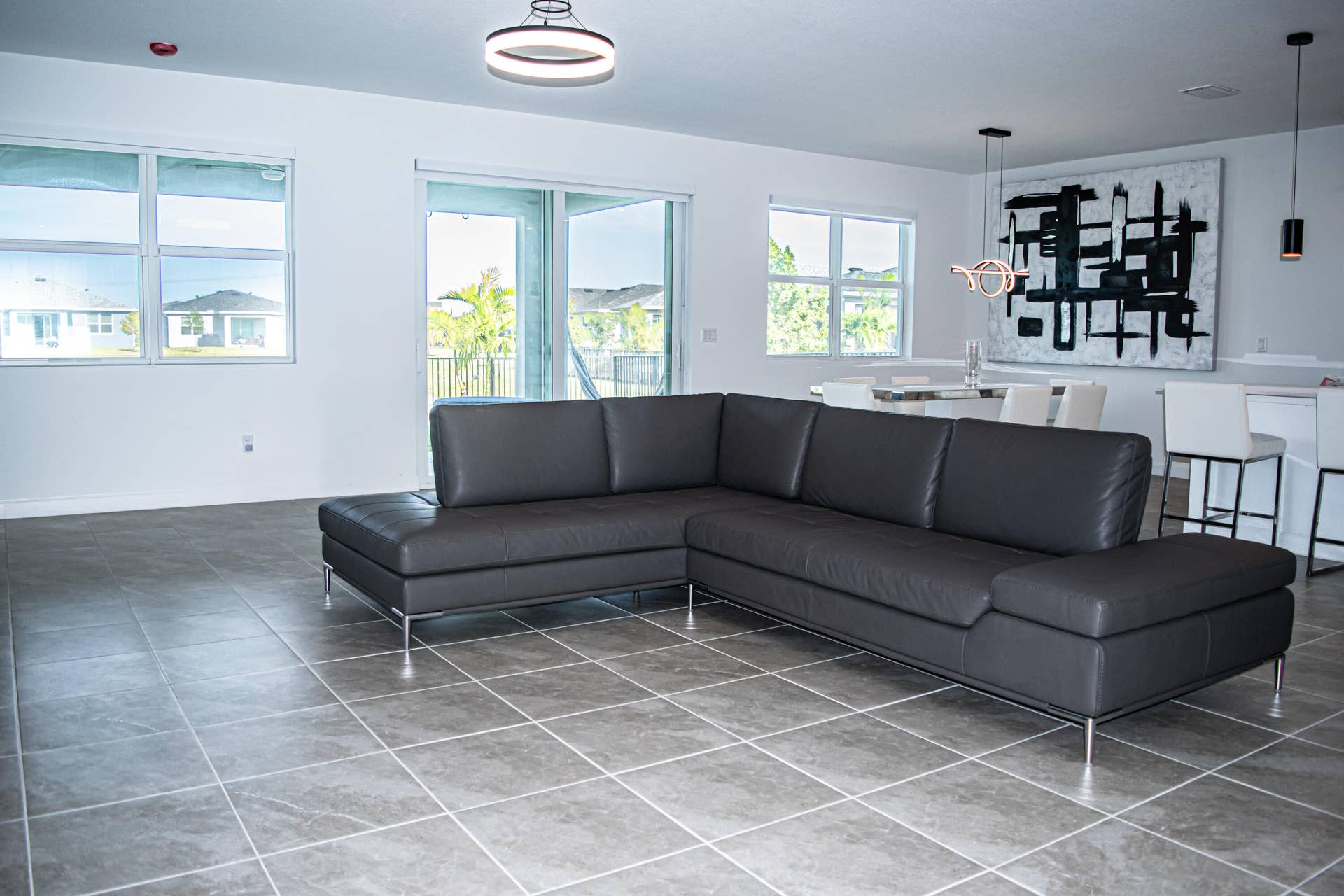 10317 SW Phineas Lane, Port St Lucie, FL 34987 Open-concept interior featuring large-format ceramic tile flooring, multiple windows, sliding glass door, and modern multi-light fixtures