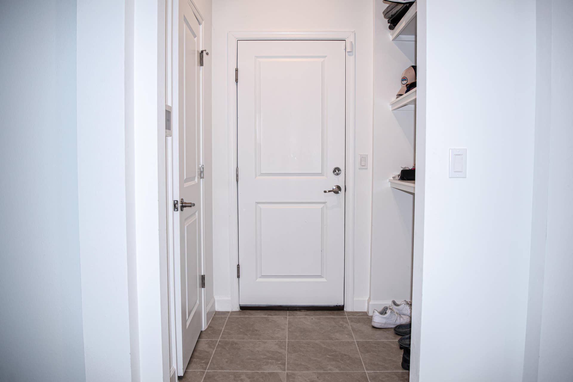 10317 SW Phineas Lane, Port St Lucie, FL 34987 Neutral-toned stone-finish tile flooring featuring a white paneled door, integrated wall shelving, and a secondary interior door with metallic hardware