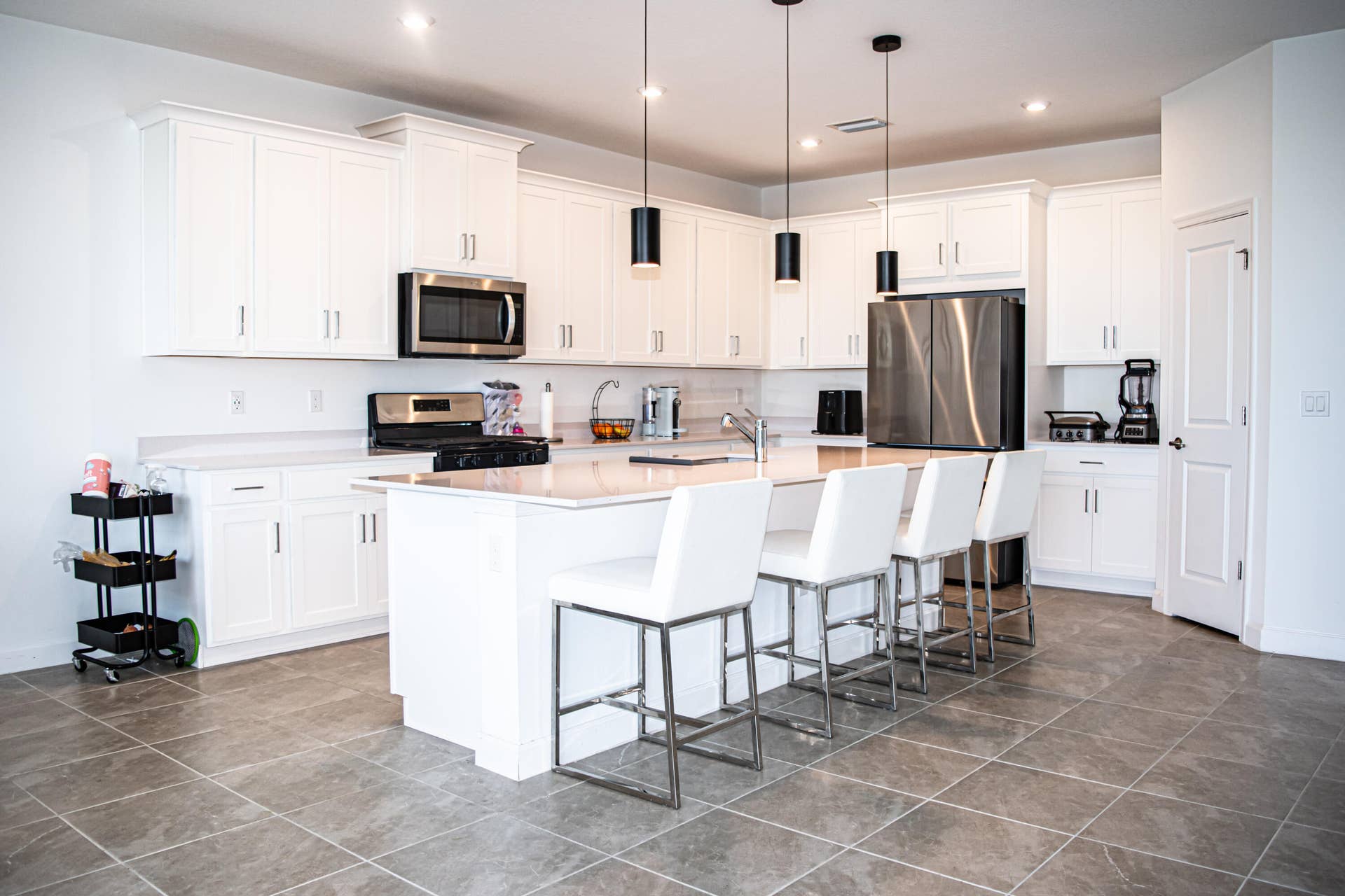 10317 SW Phineas Lane, Port St Lucie, FL 34987 Kitchen featuring white shaker-style cabinetry, a central island with a stone-finish countertop, stainless steel appliances, pendant lighting, and tile flooring