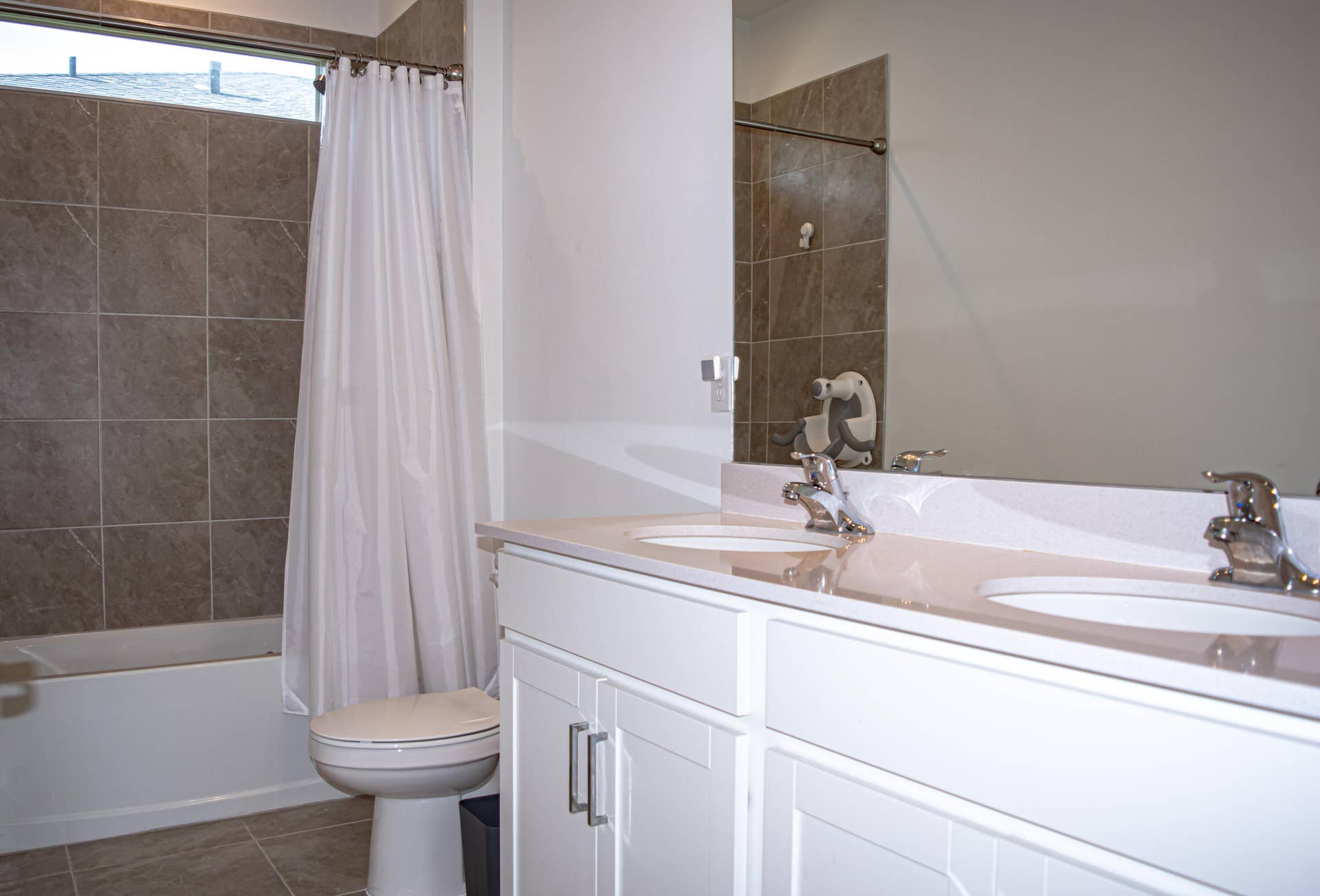 10317 SW Phineas Lane, Port St Lucie, FL 34987 Double-sink vanity with a solid-surface countertop, white cabinetry with silver hardware, full-width wall mirror, and tile-surround shower-tub combination