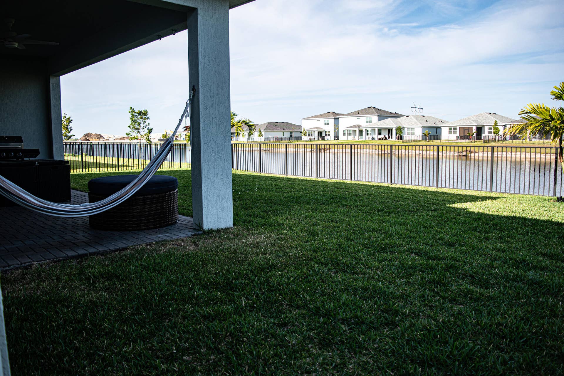 10317 SW Phineas Lane, Port St Lucie, FL 34987 Covered patio with paver flooring, manicured lawn, and aluminum perimeter fencing bordering a waterfront