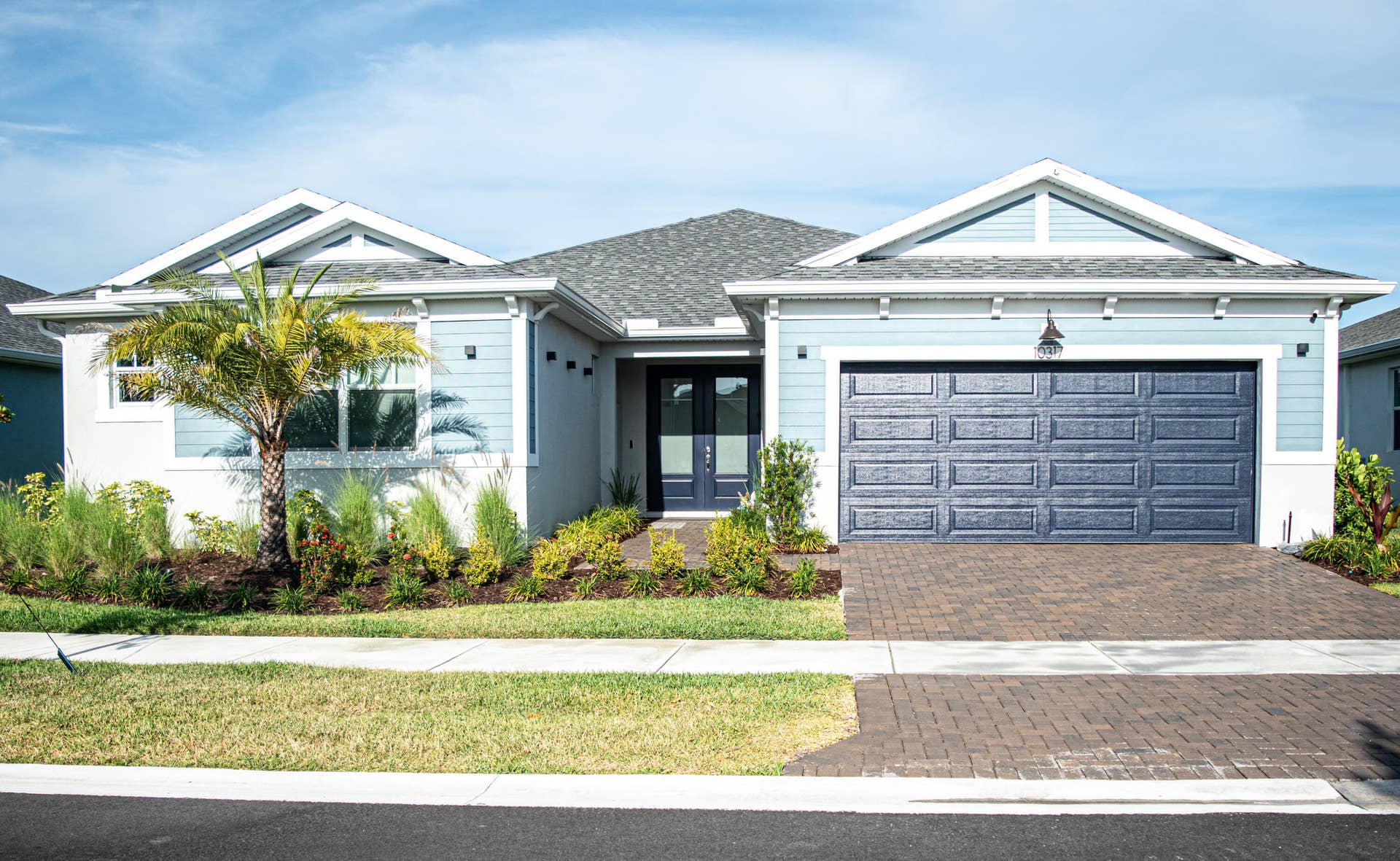 10317 SW Phineas Lane, Port St Lucie, FL 34987 Single-story exterior featuring blue horizontal lap siding, a two-car paneled garage door, a paver driveway, double front entry doors, and gable rooflines