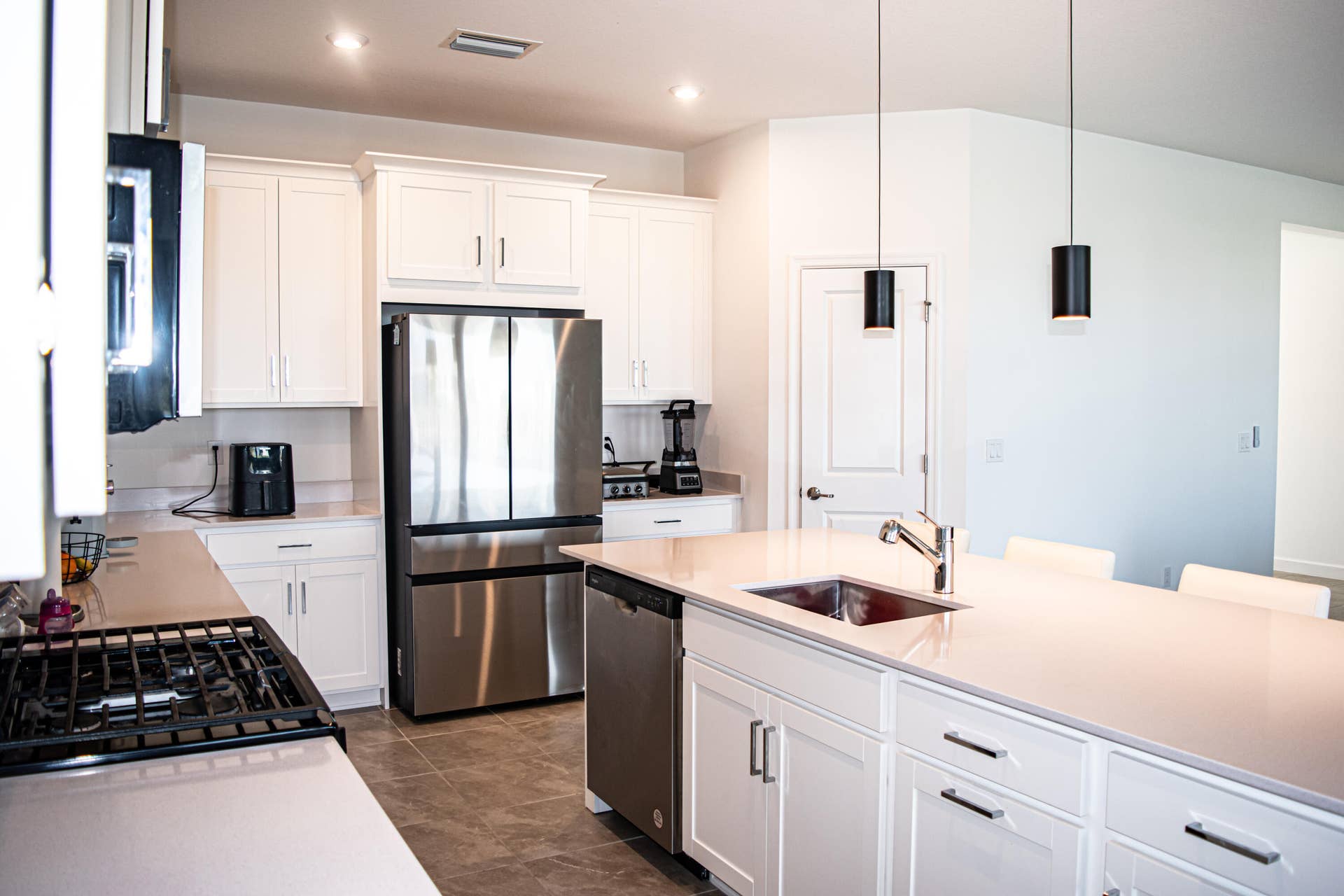 10317 SW Phineas Lane, Port St Lucie, FL 34987 Kitchen featuring white shaker-style cabinetry, a quartz-topped center island with an integrated sink, stainless steel appliances, pendant lighting, and tile flooring