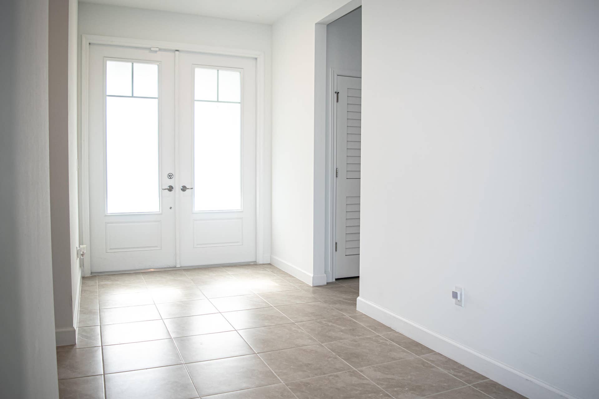 10317 SW Phineas Lane, Port St Lucie, FL 34987 Entryway featuring double glass-paneled doors, neutral tile flooring, and white interior doors with louvered accents