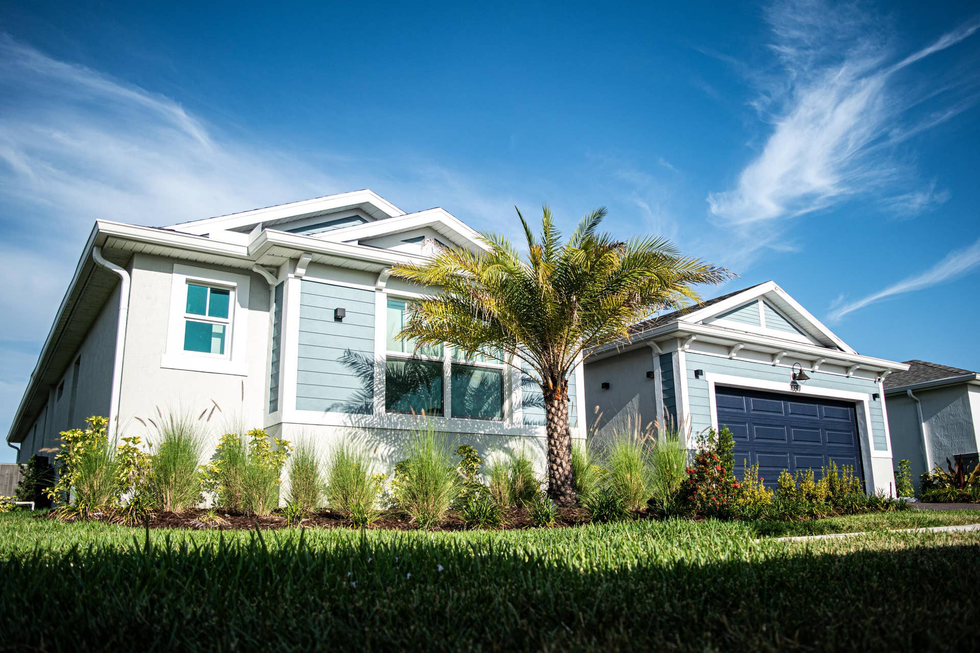 10317 SW Phineas Lane, Port St Lucie, FL 34987 Exterior featuring horizontal lap siding, a gabled roofline, an attached two-car garage, and landscaped garden beds with established ornamental grasses