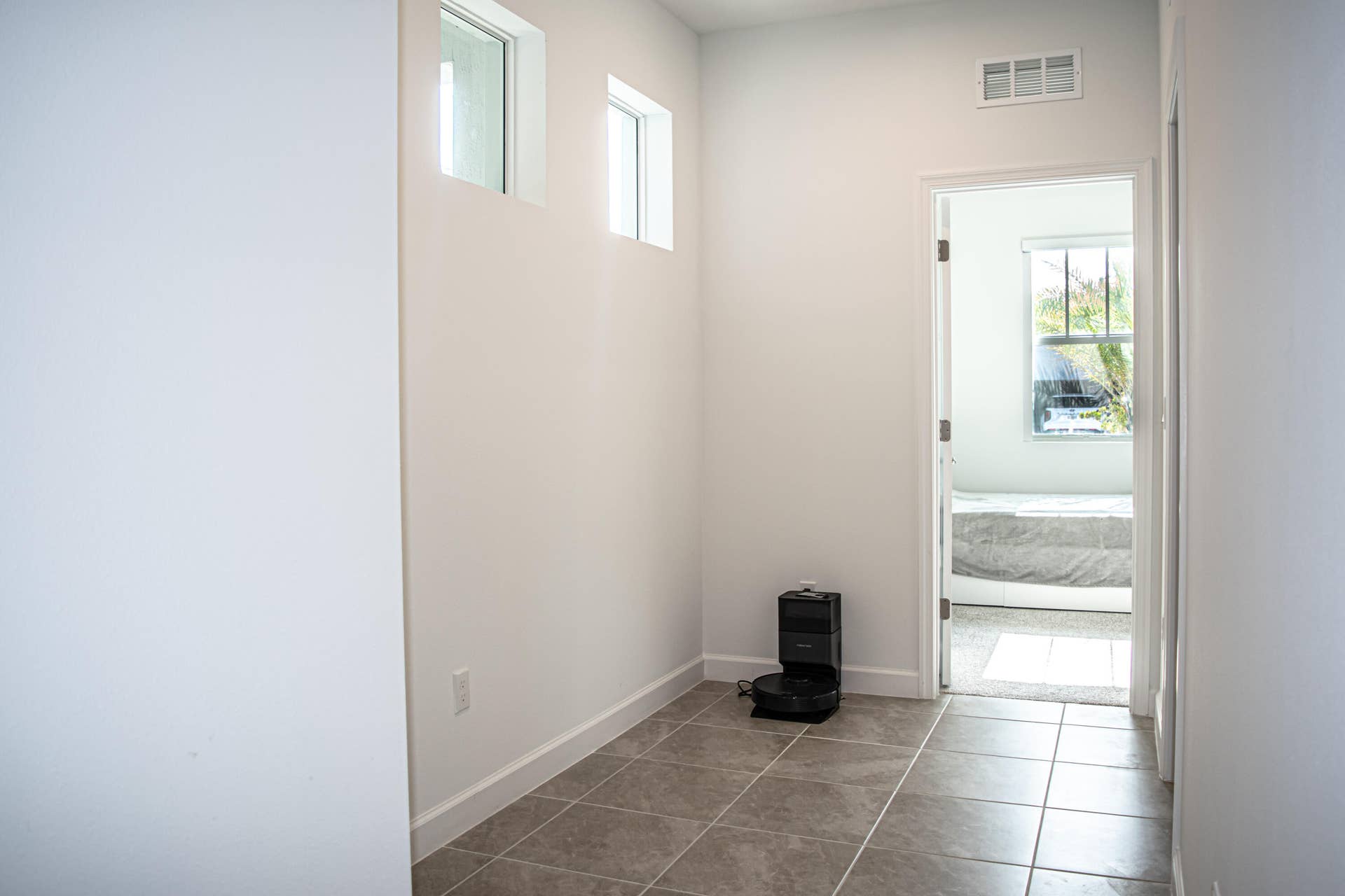 10317 SW Phineas Lane, Port St Lucie, FL 34987 Neutral-toned tile flooring, two square clerestory windows, and a doorway opening into a secondary room featuring a large window