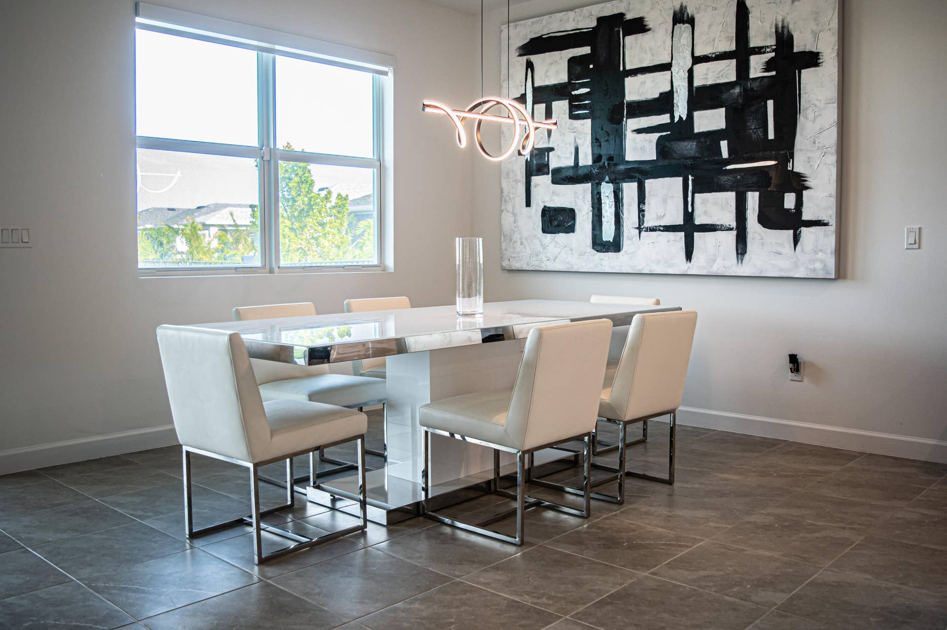 10317 SW Phineas Lane, Port St Lucie, FL 34987 Neutral-toned room featuring large-format stone-tile flooring, a window with horizontal blinds, and a contemporary sculptural LED pendant light fixture