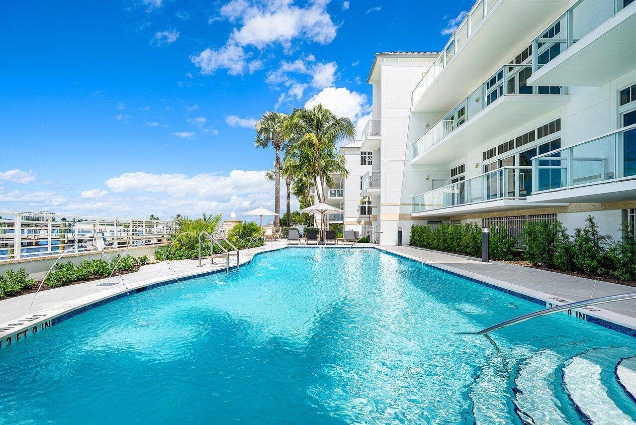 184 Lake Drive, #4201, Palm Beach Shores, FL 33404 Swimming pool with built-in stairs, metal handrails, perimeter tile detailing, stone-paver decking, and glass-paneled balconies