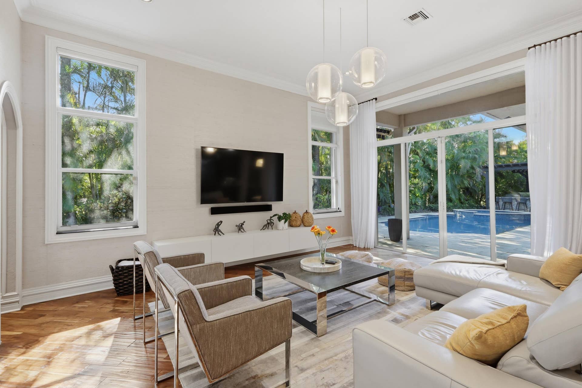 1580 VICTORIA ISLE Way, Weston, FL 33327 Living area featuring wood-finish flooring, multi-light glass pendant fixture, crown molding, and large-format glass sliding doors opening to an outdoor pool area