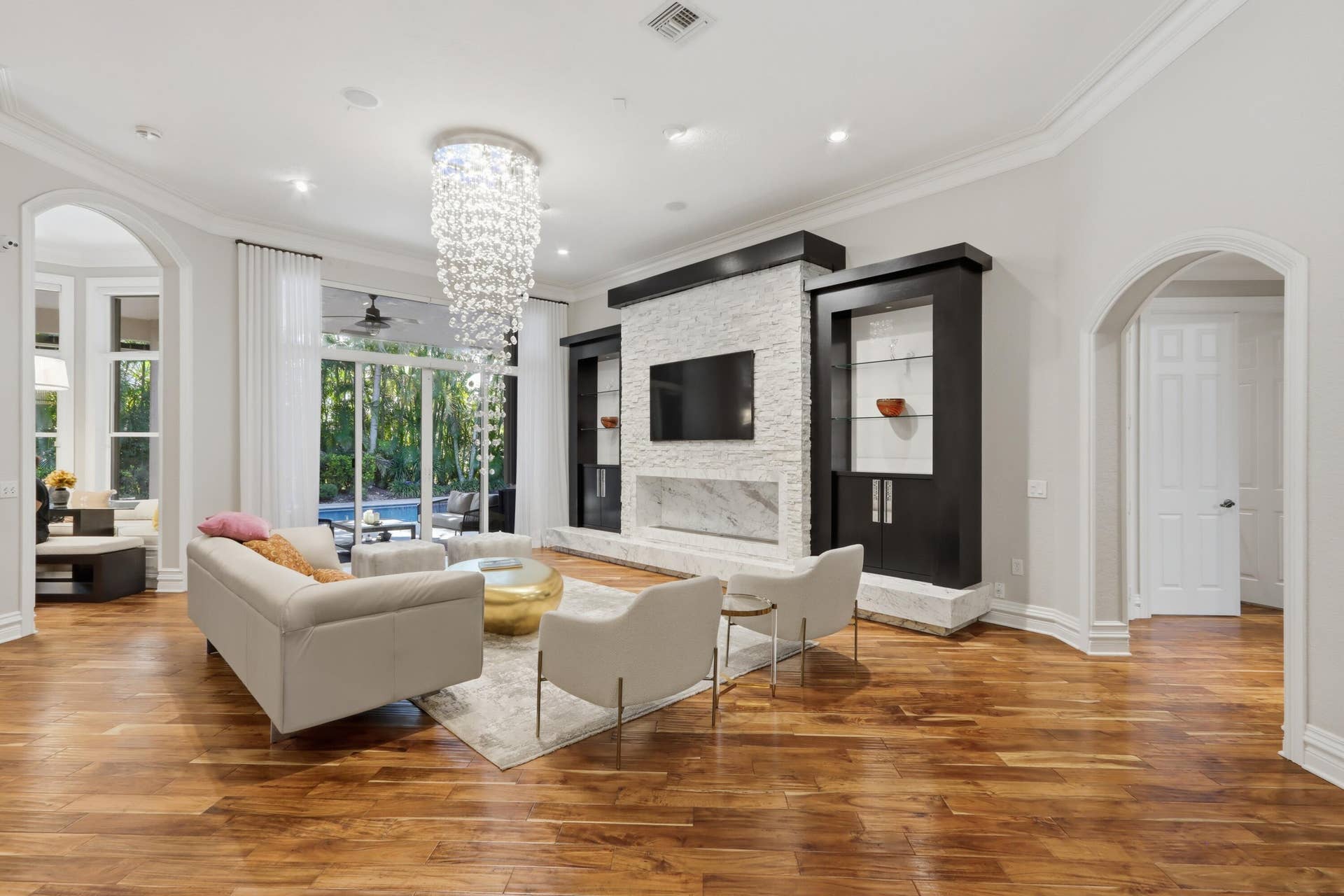1580 VICTORIA ISLE Way, Weston, FL 33327 Formal living space featuring wood-finish flooring, a floor-to-ceiling stone-textured fireplace with built-in dark wood cabinetry, an intricate crystal chandelier, and arched entryways
