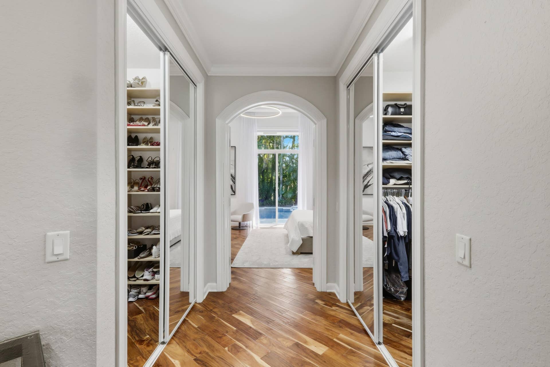 1580 VICTORIA ISLE Way, Weston, FL 33327 His and Hers walk-in wardrobe featuring mirrored sliding doors, custom integrated shelving, wood-finish flooring, and a decorative arched entryway
