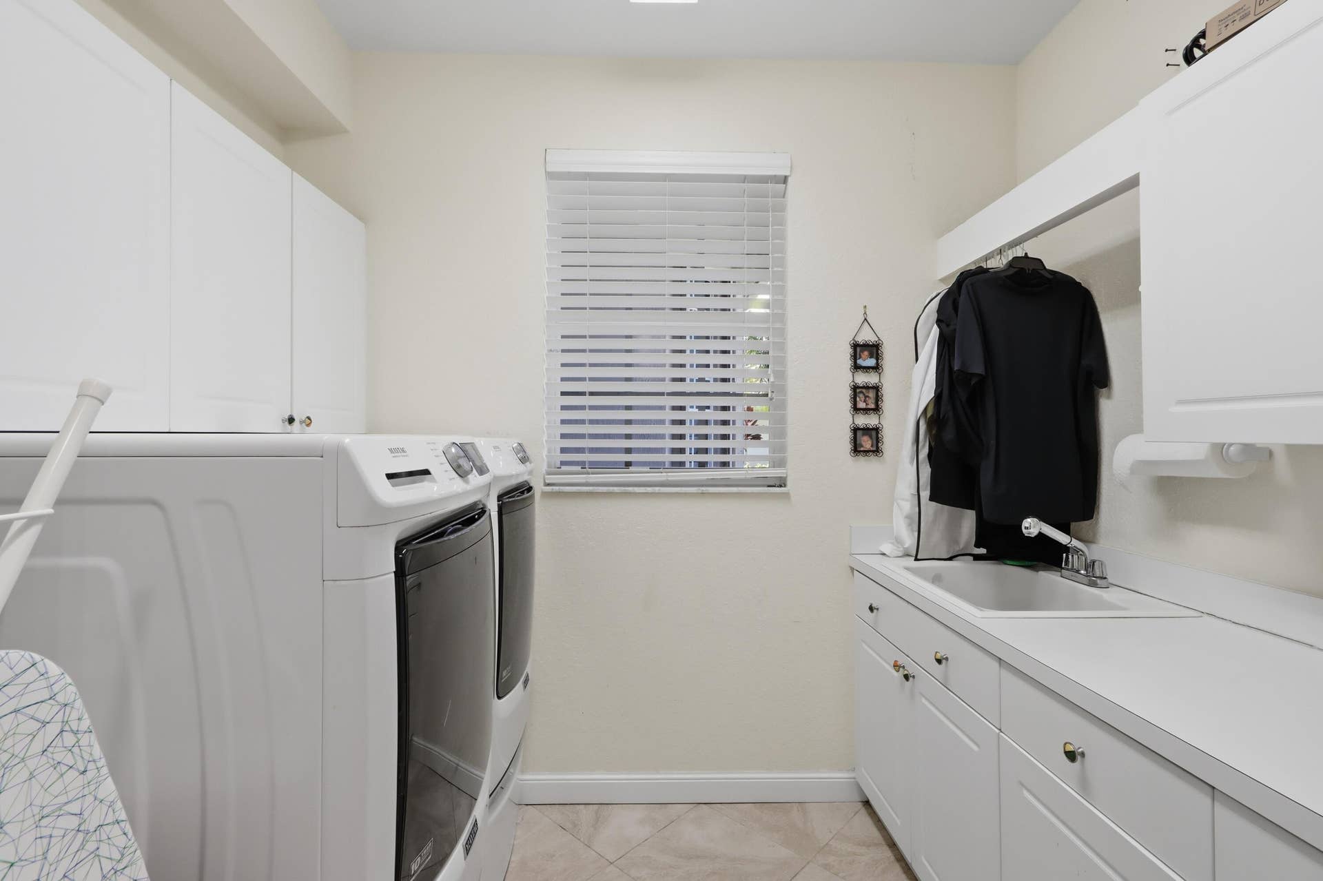 1580 VICTORIA ISLE Way, Weston, FL 33327 Laundry area featuring white shaker-style cabinetry, a drop-in utility sink with a chrome faucet, solid-surface countertops, and a window with horizontal blinds