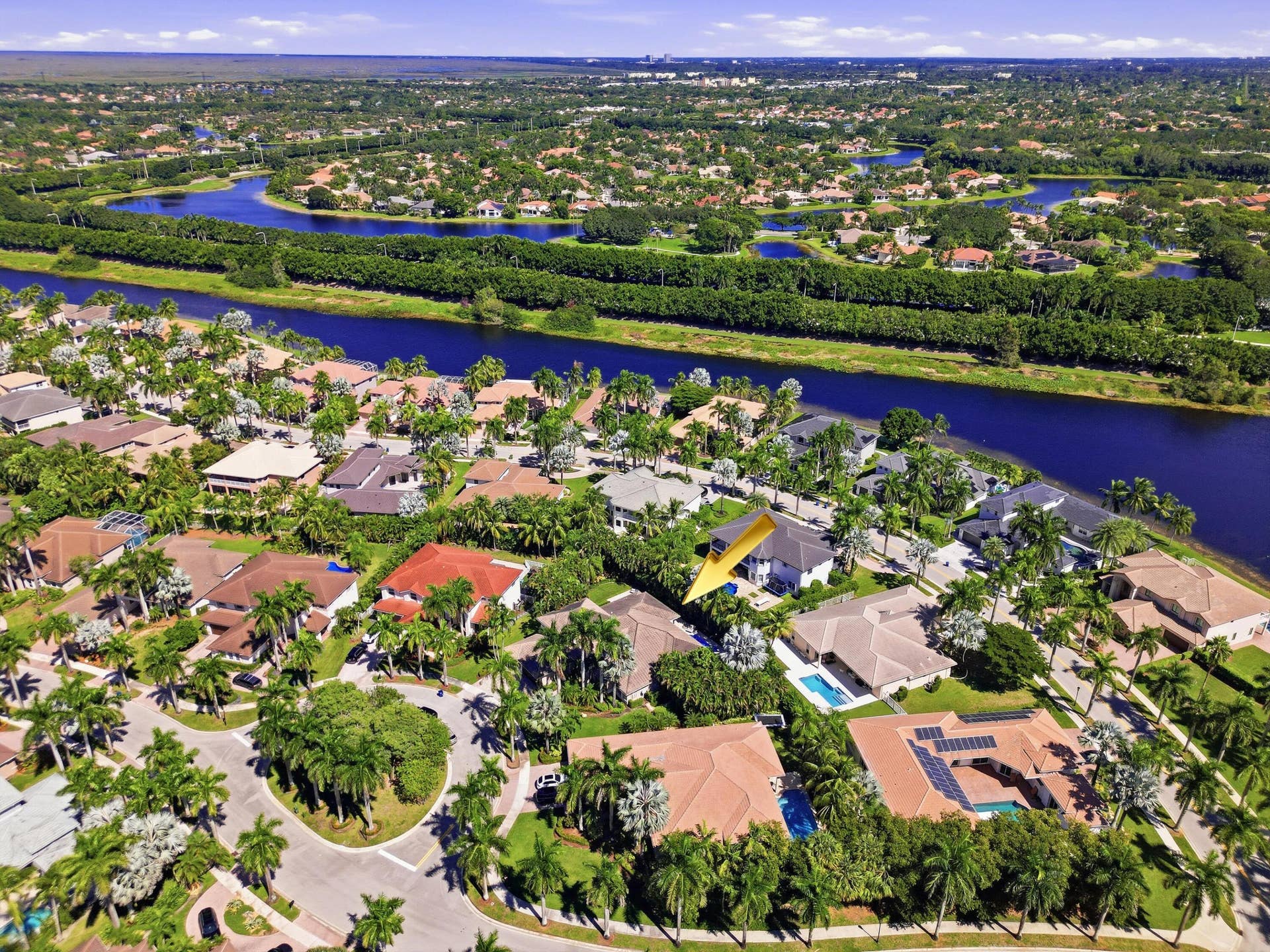 1580 VICTORIA ISLE Way, Weston, FL 33327 Aerial perspective of a residential property situated in a suburban community featuring canal-side positioning, mature palm trees, and terracotta-style roof tiles