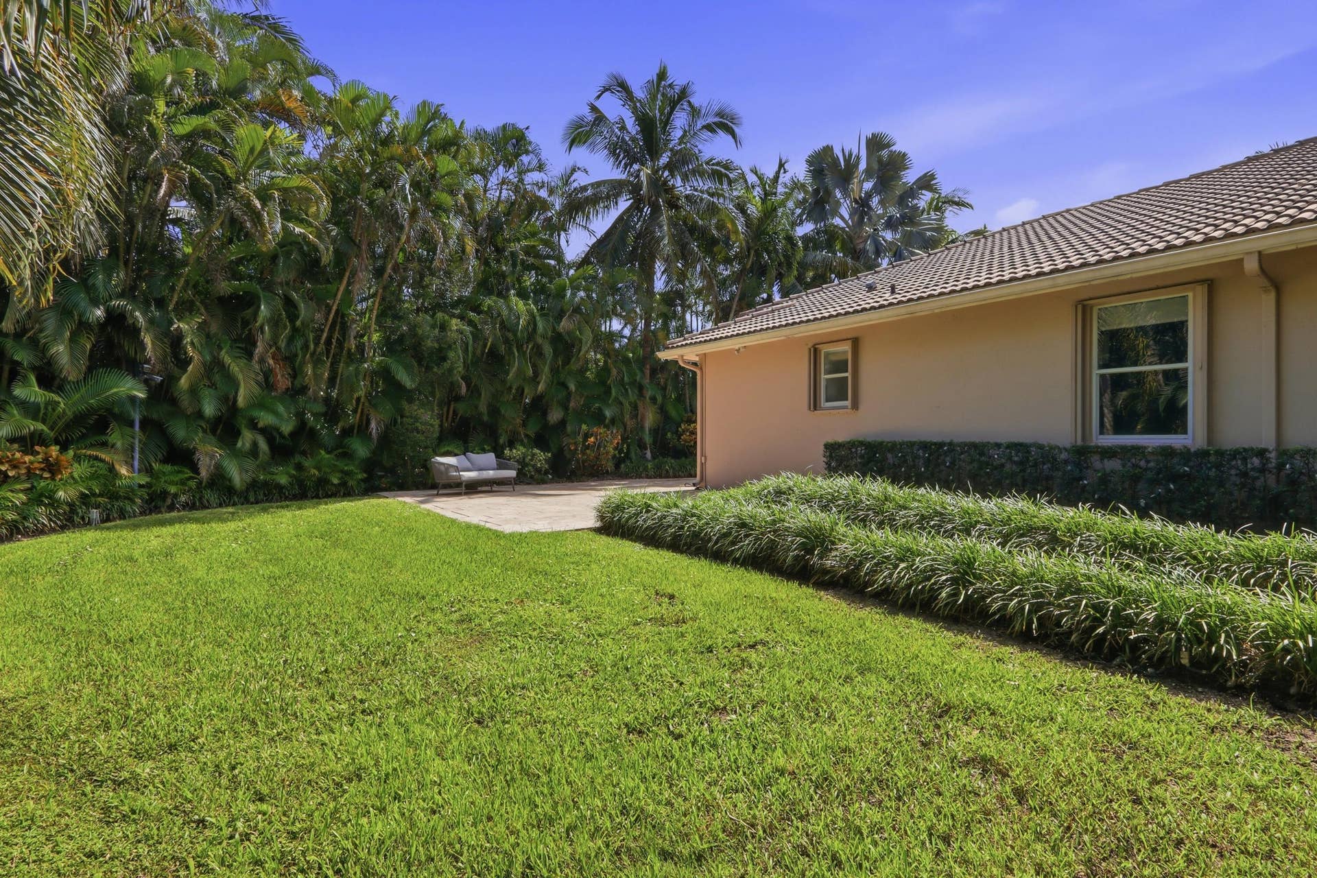 1580 VICTORIA ISLE Way, Weston, FL 33327 Rear yard featuring a manicured lawn, paved patio, mature palm trees, and established shrubbery bordering the stucco exterior with tile roofing