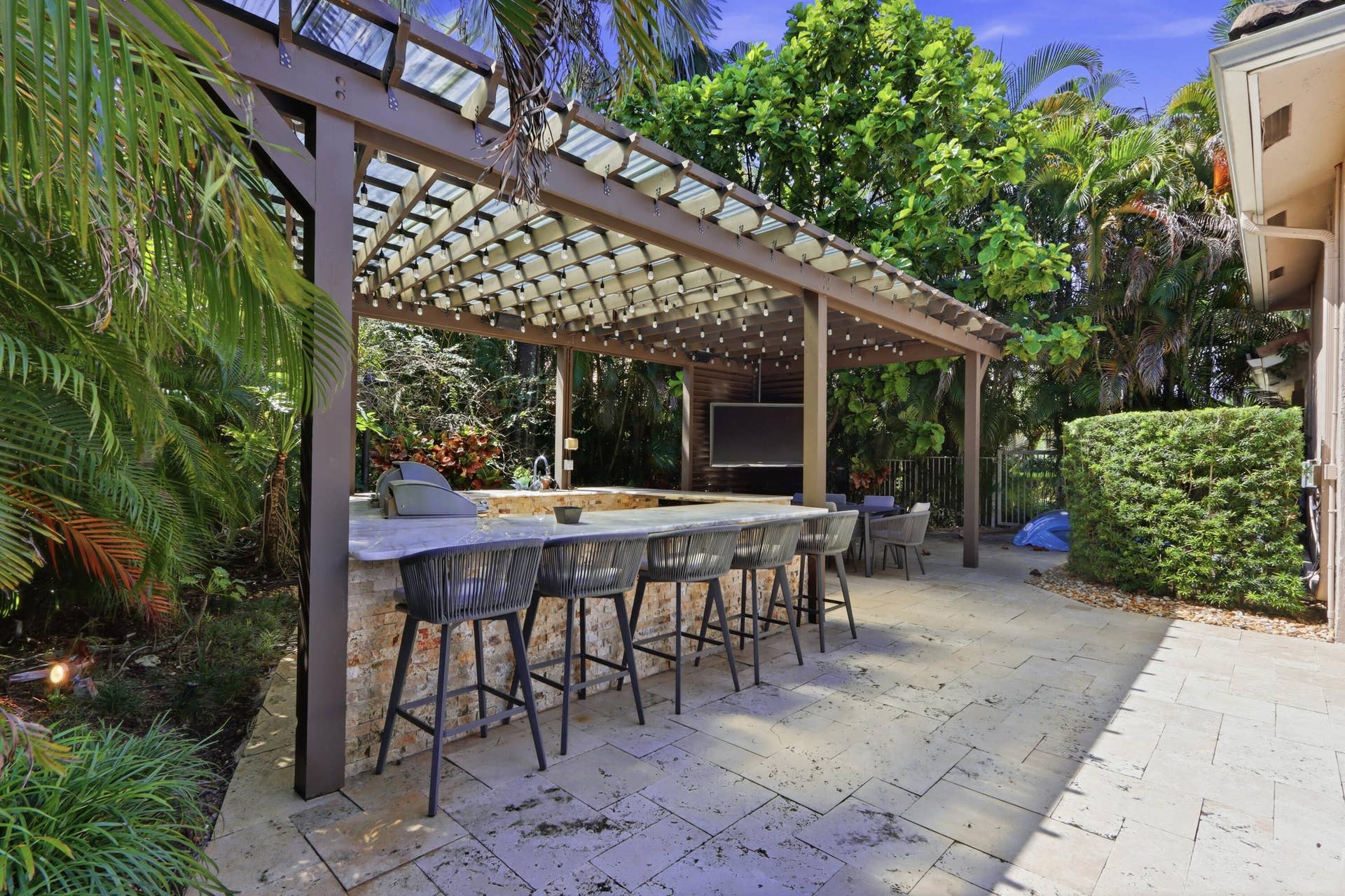 1580 VICTORIA ISLE Way, Weston, FL 33327 Outdoor kitchen area featuring a stone-clad bar, integrated grill, stone-tile patio, and a pergola with a slatted roof structure