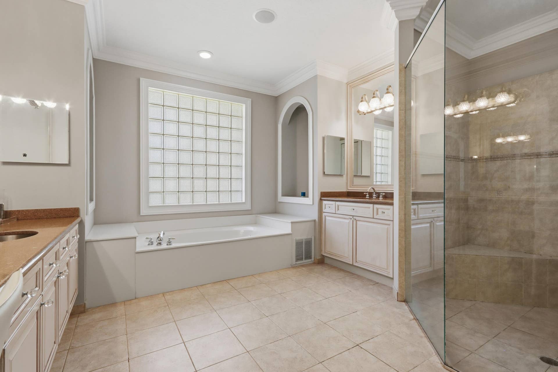 1580 VICTORIA ISLE Way, Weston, FL 33327 Bathroom featuring a soaking tub, glass block window, stone-tiled walk-in shower with bench, dual vanities with stone countertops, and arched wall niche