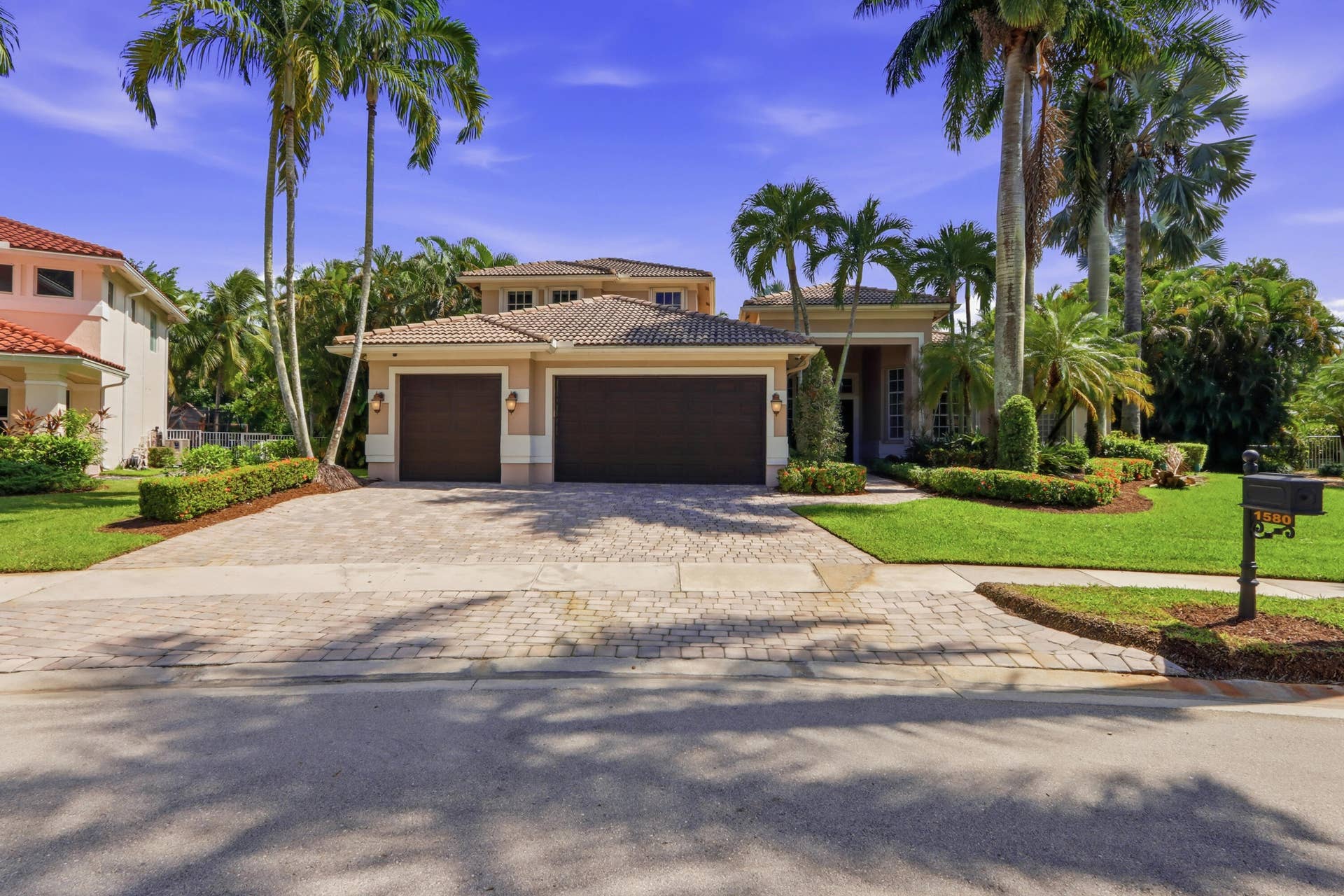 1580 VICTORIA ISLE Way, Weston, FL 33327 Multi-hipped tile roof, a three-car garage, and a paved stone driveway surrounded by manicured landscaping and mature palm trees