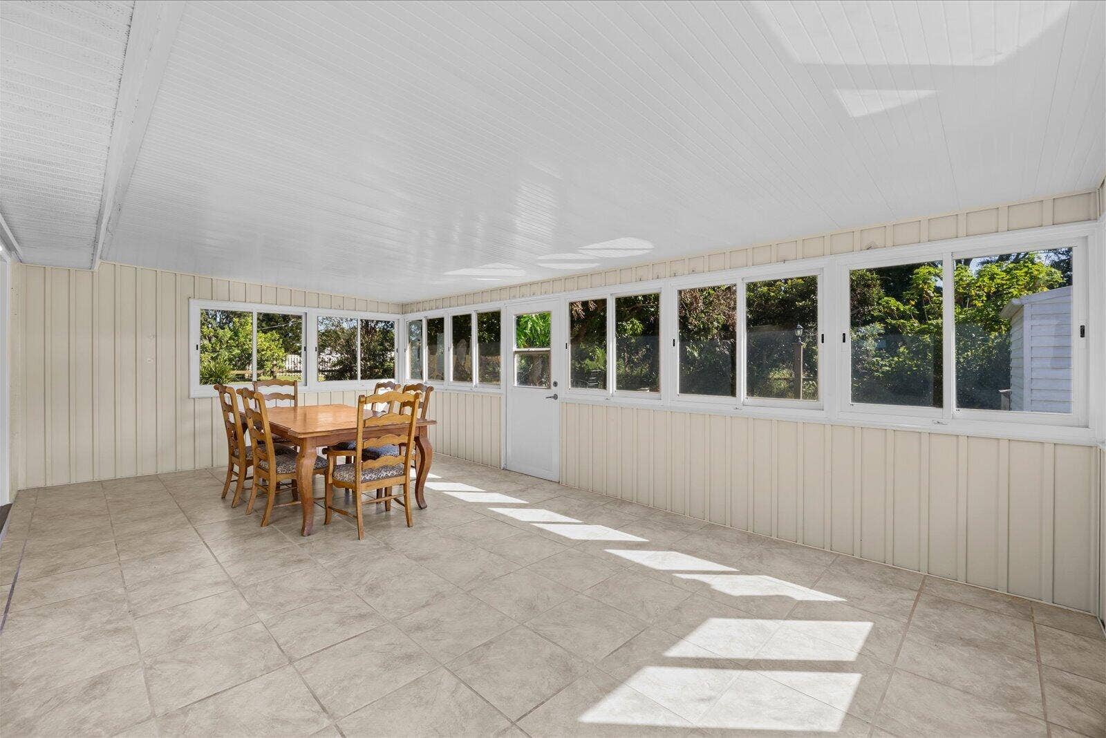 113 CONOVER Avenue, Sebastian, FL 32958 Enclosed sunroom featuring large paneled windows, neutral tile flooring, light-toned vertical paneling, and a painted beadboard ceiling