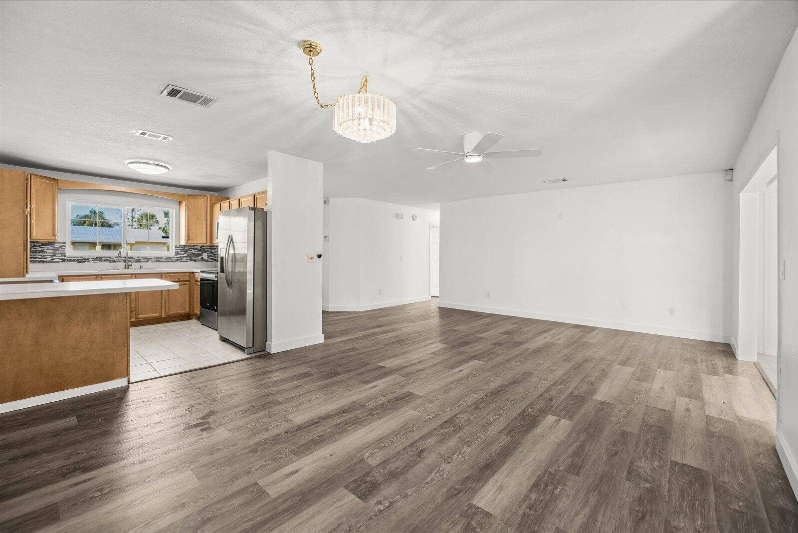 113 CONOVER Avenue, Sebastian, FL 32958 Open-concept interior featuring wood-finish flooring, a kitchen with light-tone cabinetry, stainless steel appliances, a crystal-style chandelier, and a white ceiling fan