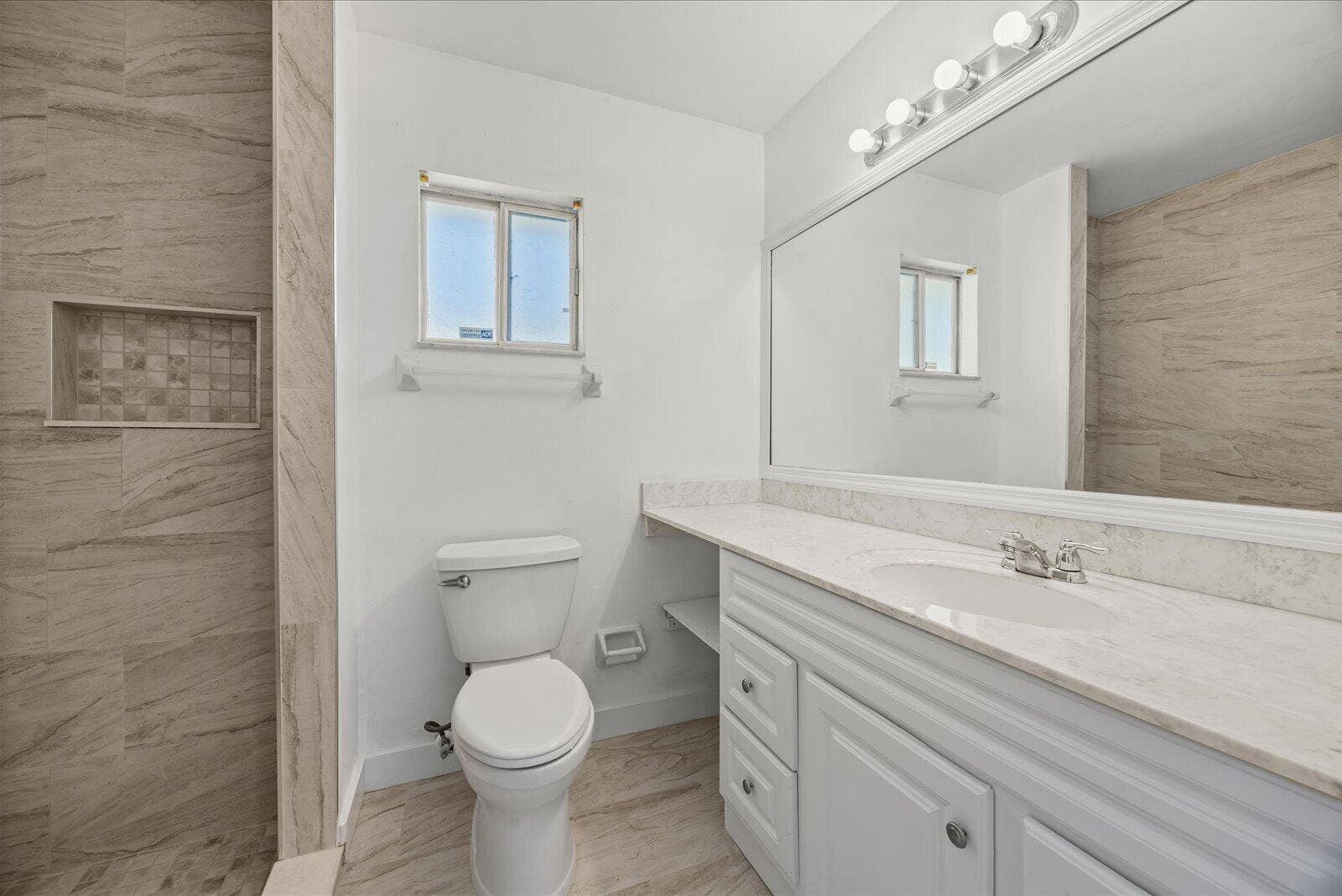 113 CONOVER Avenue, Sebastian, FL 32958 Bathroom featuring a vanity with stone-finish countertop, full-width wall mirror, wood-finish flooring, and a shower enclosure with tile surround and built-in recessed shelving