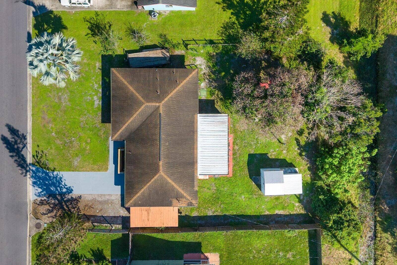 113 CONOVER Avenue, Sebastian, FL 32958 Aerial perspective of property featuring a hip-style roof, a paved driveway, a metal-covered patio, a detached storage structure, and expansive grass landscaping