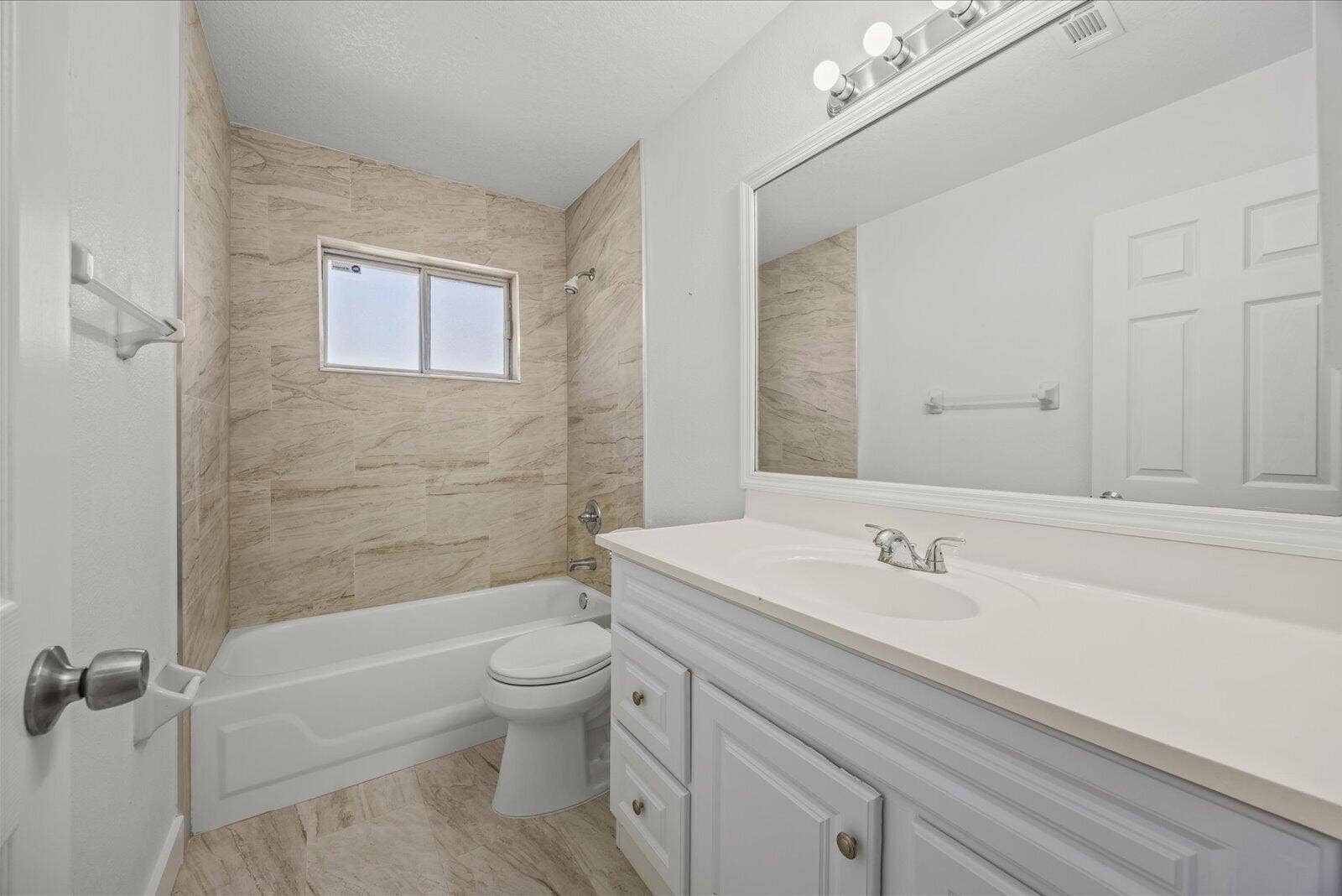 113 CONOVER Avenue, Sebastian, FL 32958 Bathroom featuring a white vanity with an integrated basin, large wall-mounted mirror, three-bulb vanity lighting, and a tub-shower combination enclosed by neutral-toned tiled walls