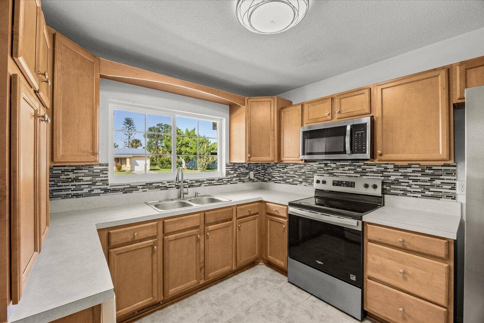 113 CONOVER Avenue, Sebastian, FL 32958 Kitchen featuring natural wood cabinetry, stainless steel appliances, a multi-tone tile backsplash, and solid surface countertops with a dual-basin sink