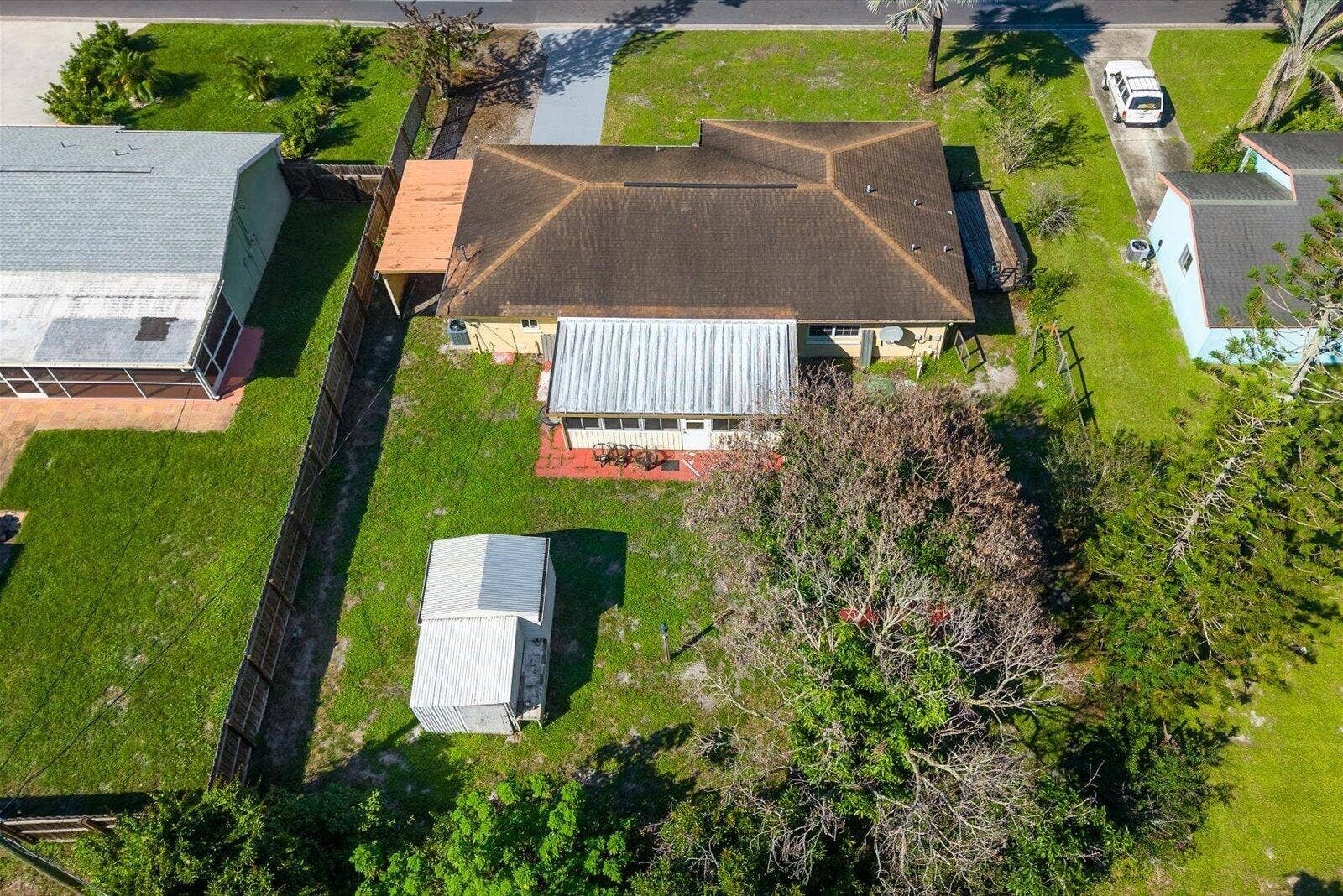 113 CONOVER Avenue, Sebastian, FL 32958 Aerial perspective of a detached property featuring a hip roof, a covered patio with a metal awning, an attached side carport, and a detached metal storage structure situated within a fenced rear lot