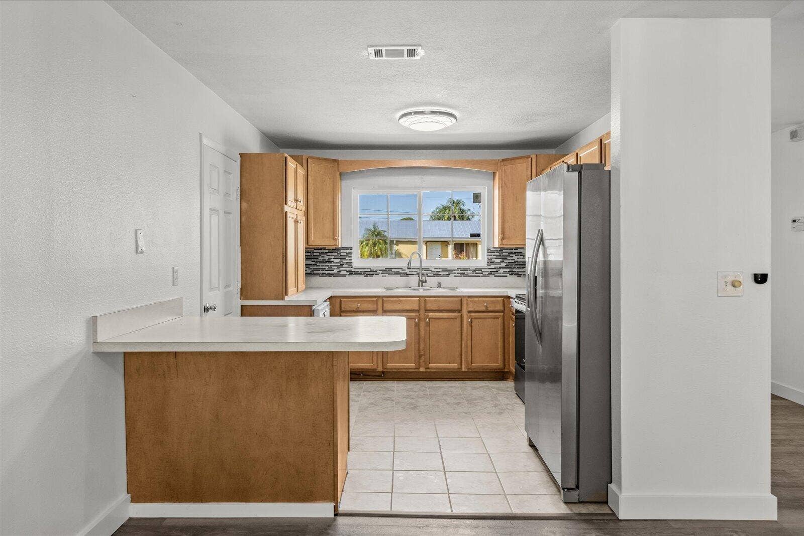 113 CONOVER Avenue, Sebastian, FL 32958 Kitchen featuring wood cabinetry, stone-style tile backsplash, white countertops, tile flooring, and stainless steel refrigerator