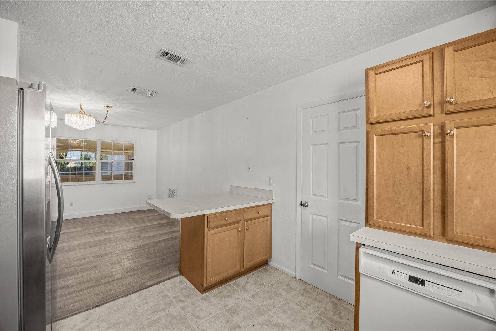 113 CONOVER Avenue, Sebastian, FL 32958 Kitchen featuring light wood-finish cabinetry, a peninsula with a solid-surface countertop, stainless steel refrigerator, white dishwasher, and wood-finish flooring