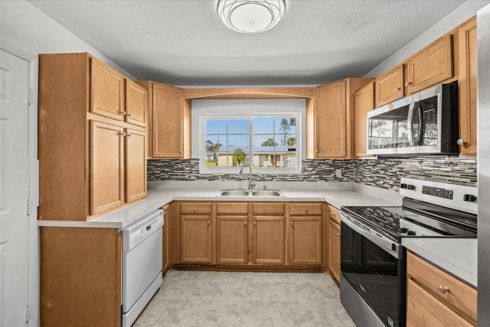 113 CONOVER Avenue, Sebastian, FL 32958 Kitchen featuring wood cabinetry, solid-surface countertops, decorative stone-style tile backsplash, stainless steel microwave, and dual-basin sink with arched-neck faucet