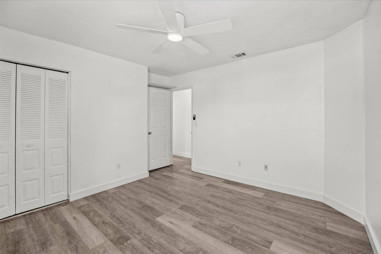 113 CONOVER Avenue, Sebastian, FL 32958 Neutral-toned room featuring wood-finish flooring, a white five-blade ceiling fan with integrated lighting, and louvered double-door closet cabinetry