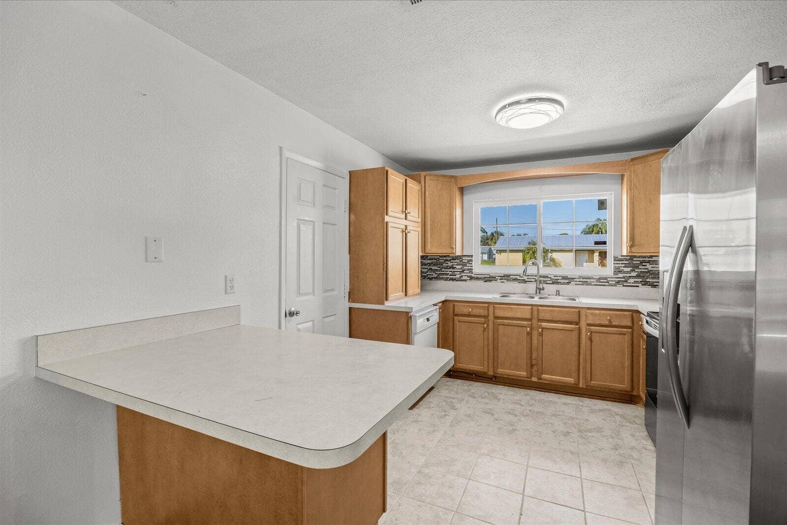 113 CONOVER Avenue, Sebastian, FL 32958 Kitchen featuring wood cabinetry, solid-surface countertops, tile backsplash, stainless steel refrigerator, and tiled flooring