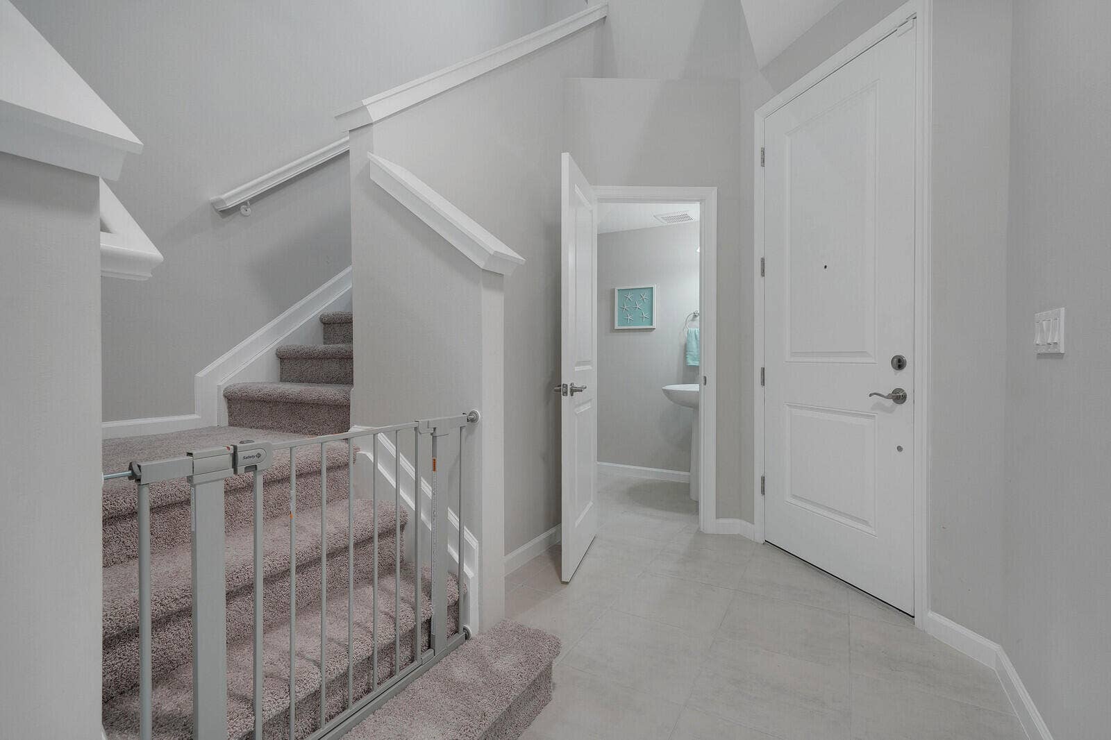 Foyer featuring tile flooring, a paneled front door with metallic hardware, and a carpeted staircase with a white handrail
