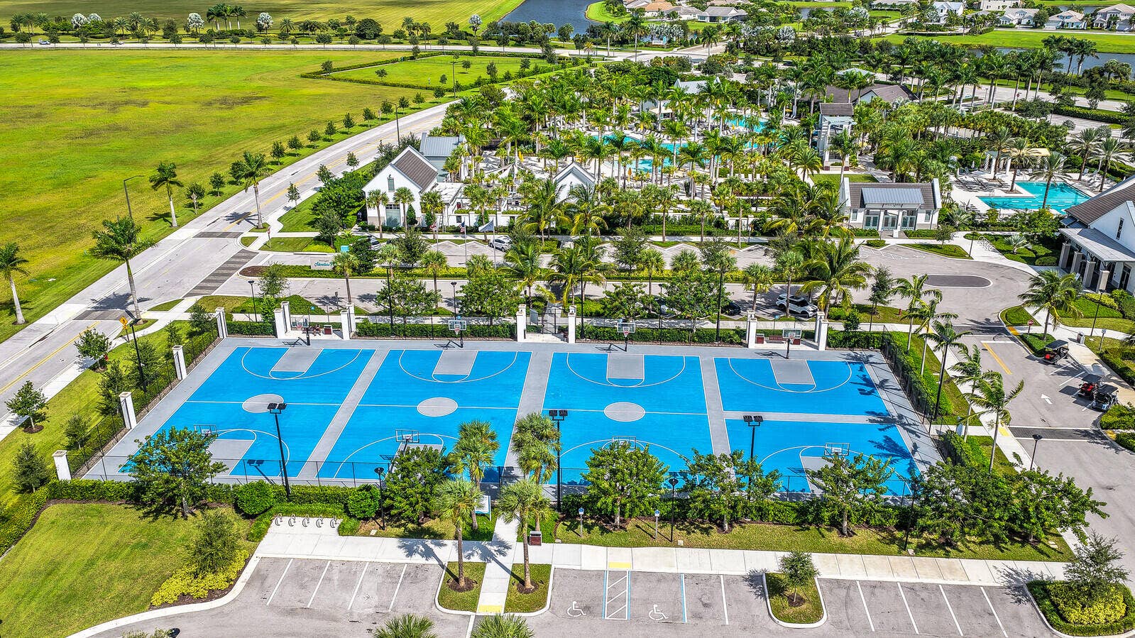 Outdoor athletic facility featuring multiple basketball courts with blue surfacing, perimeter fencing, and integrated lighting fixtures