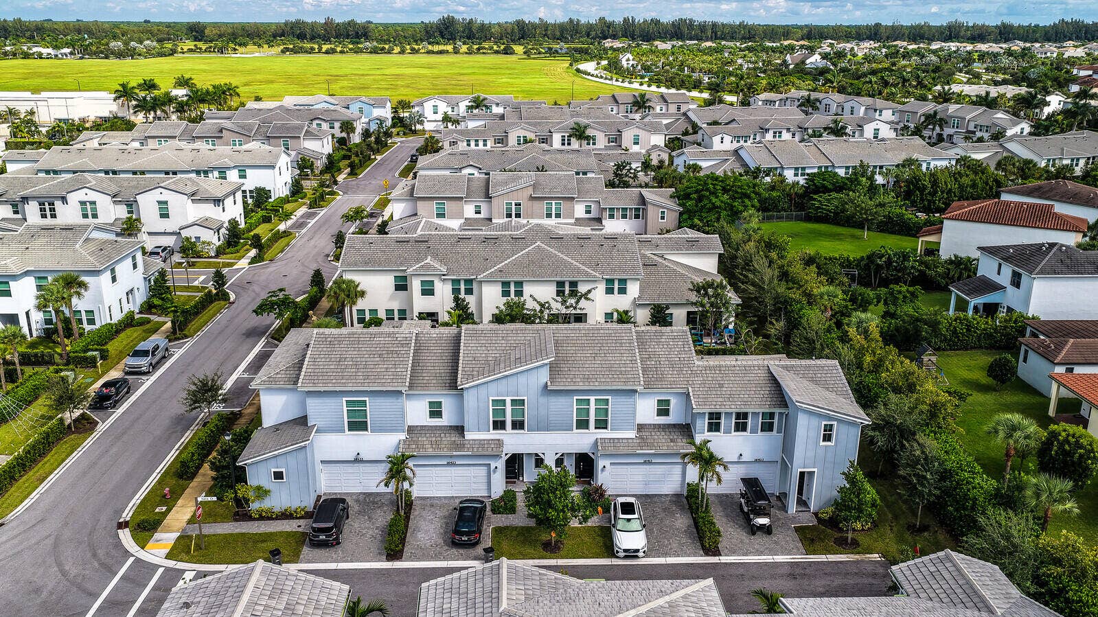 Multi-unit residential complex featuring gabled rooflines, light-toned horizontal siding, paved driveways, and integrated garage doors