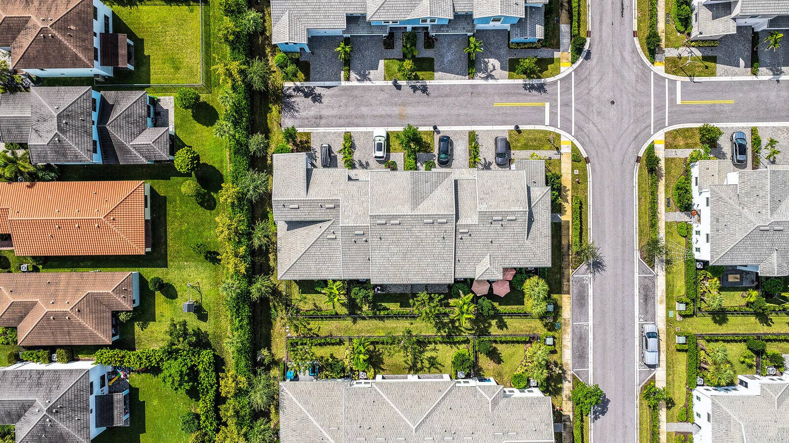 Aerial perspective of a multi-unit residential property featuring a shingle roof, concrete-paved motor court, and landscaped perimeter hedges
