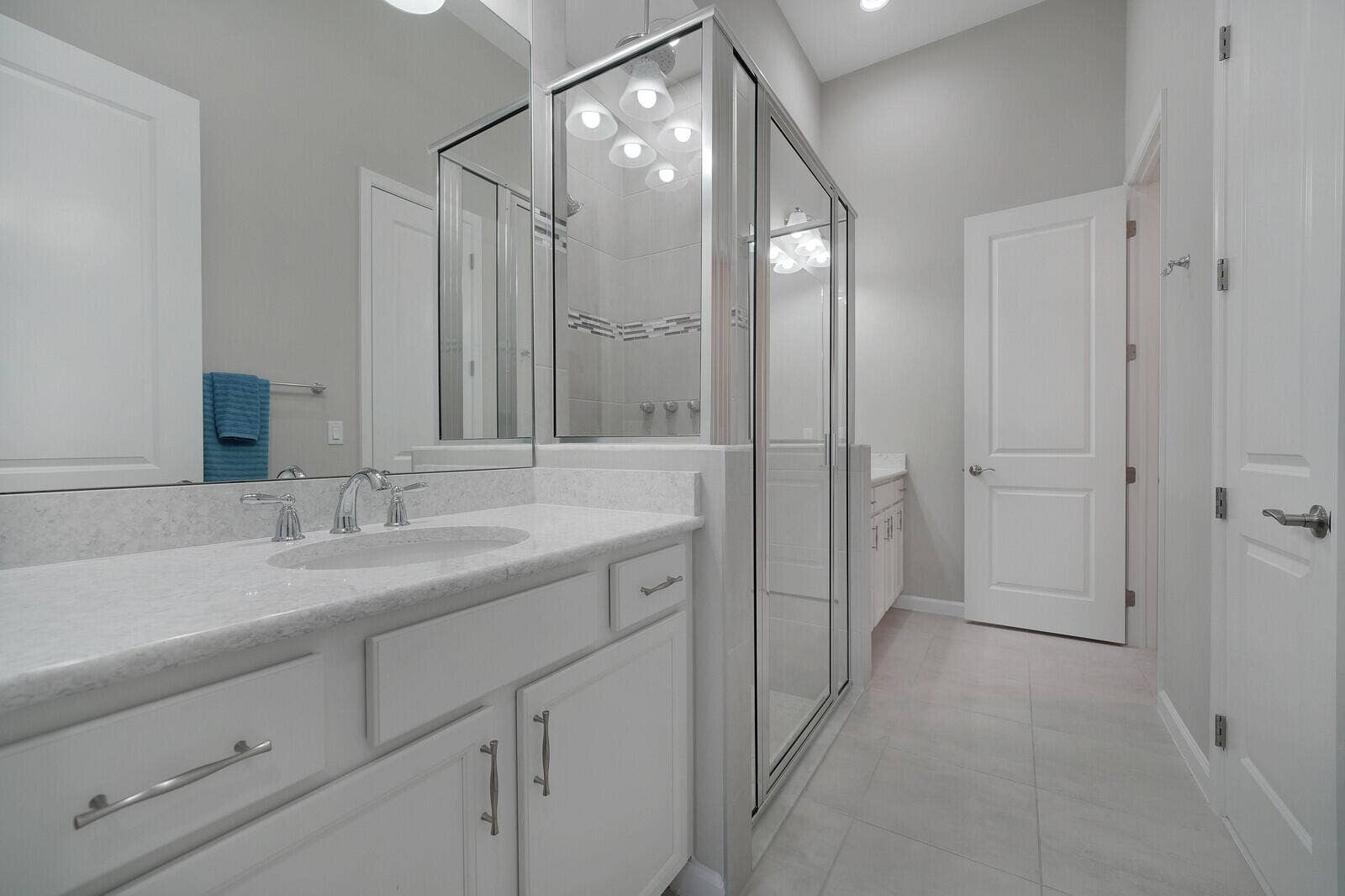 Large Ensuite Primary Bathroom with Dual Sinks, Walk in Closet, Linen Closet, White cabinetry with brushed nickel hardware, Quartz countertops, undermount sink, and glass-enclosed shower with tile surround.