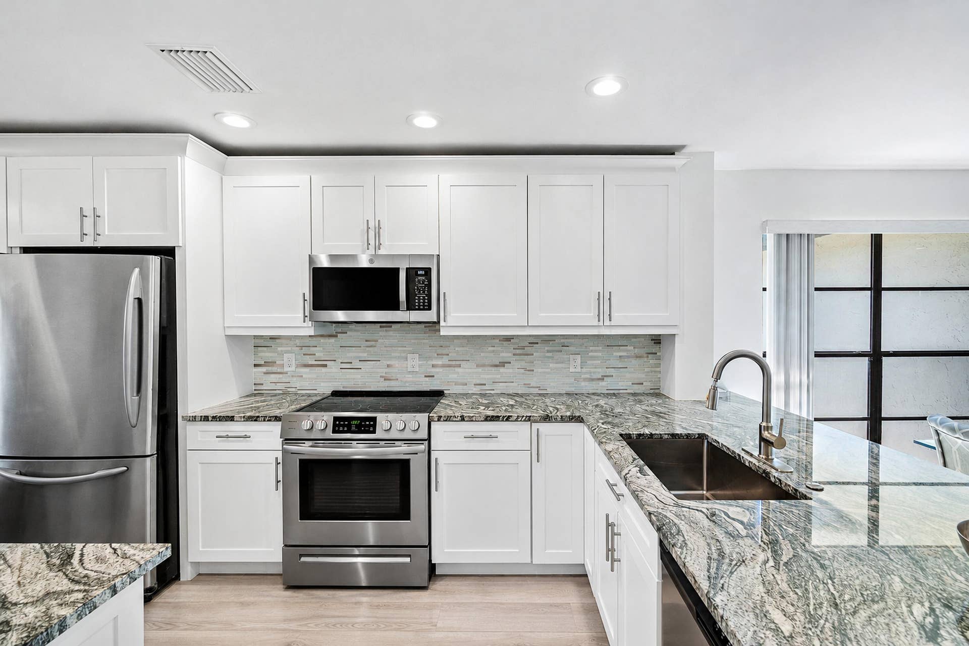 21 Southport Lane, #B, Boynton Beach, FL 33436 Kitchen featuring white shaker-style cabinetry, patterned stone countertops, stainless steel appliances, a multi-tonal linear tile backsplash, and an undermount stainless steel sink with a high-arc faucet