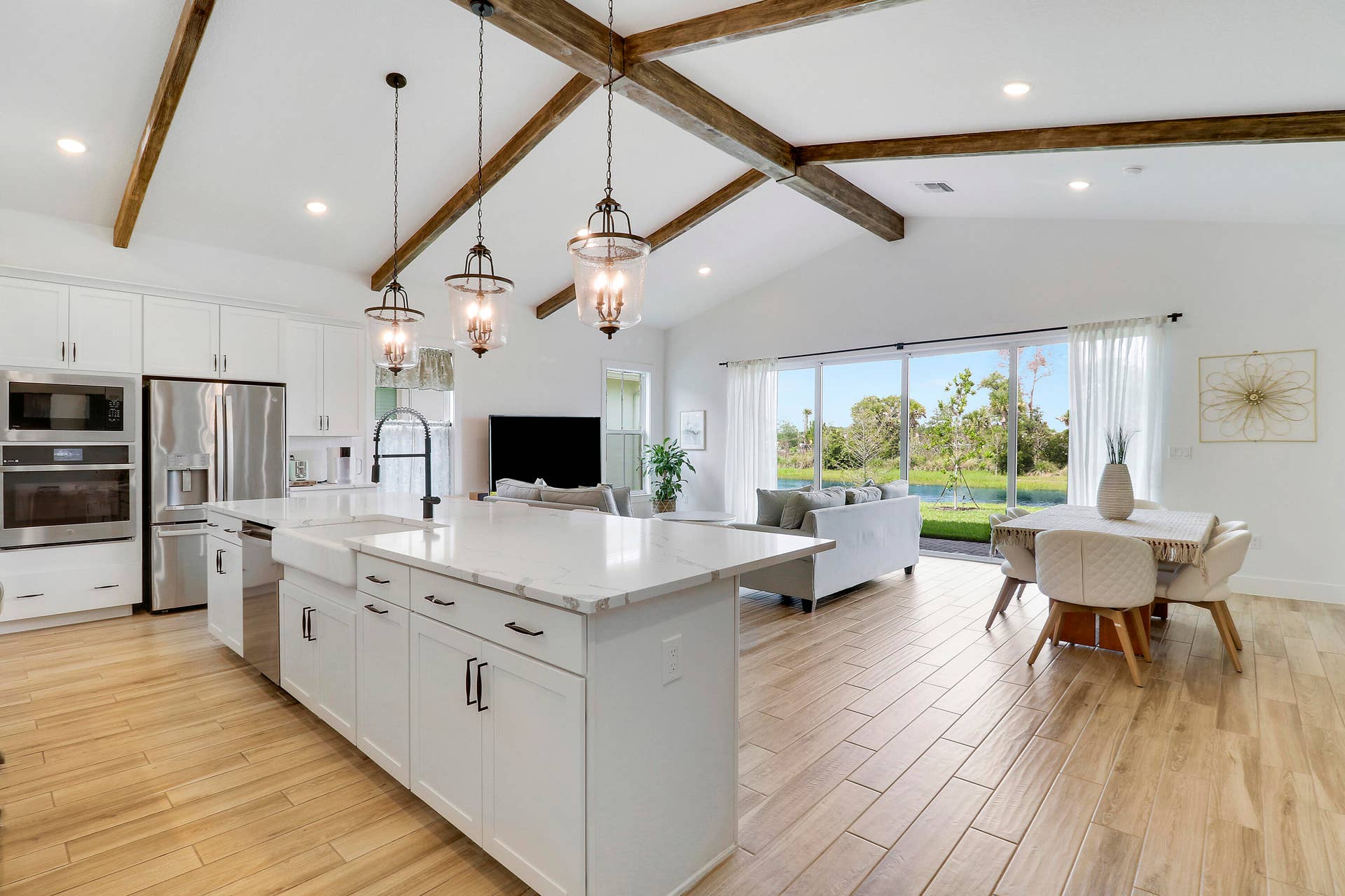 6742 SE LOST PINE Drive, Stuart, FL 34997 Kitchen featuring vaulted ceilings imitating wood beams, an expansive center island with a farmhouse-style sink, quartz countertops, pendant lighting, and wood-finish tile flooring