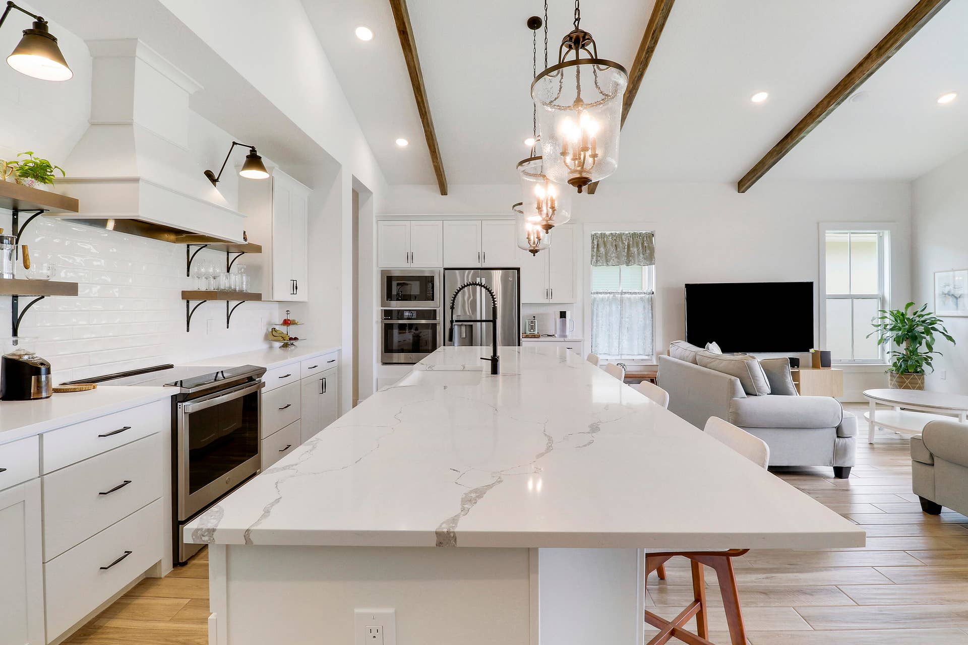 6742 SE LOST PINE Drive, Stuart, FL 34997 Kitchen featuring a central island with a stone countertop, white shaker cabinetry, stainless steel built-in appliances, decorative ceiling beams, and tile wood like flooring