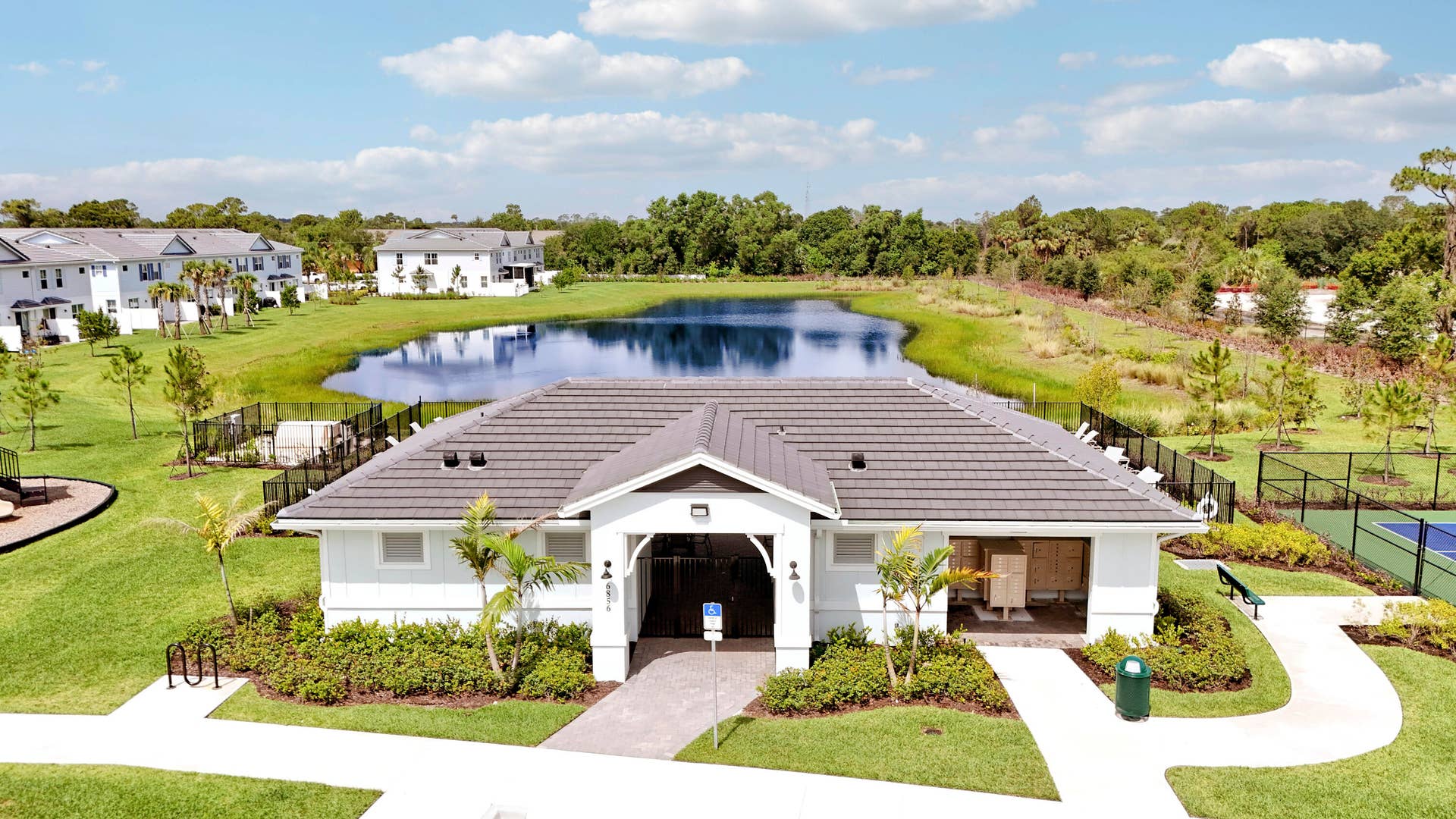 6742 SE LOST PINE Drive, Stuart, FL 34997 Community clubhouse featuring a dark tile roof, exterior lighting fixtures, and a paved walkway, situated on grounds with a retention pond and sport court.